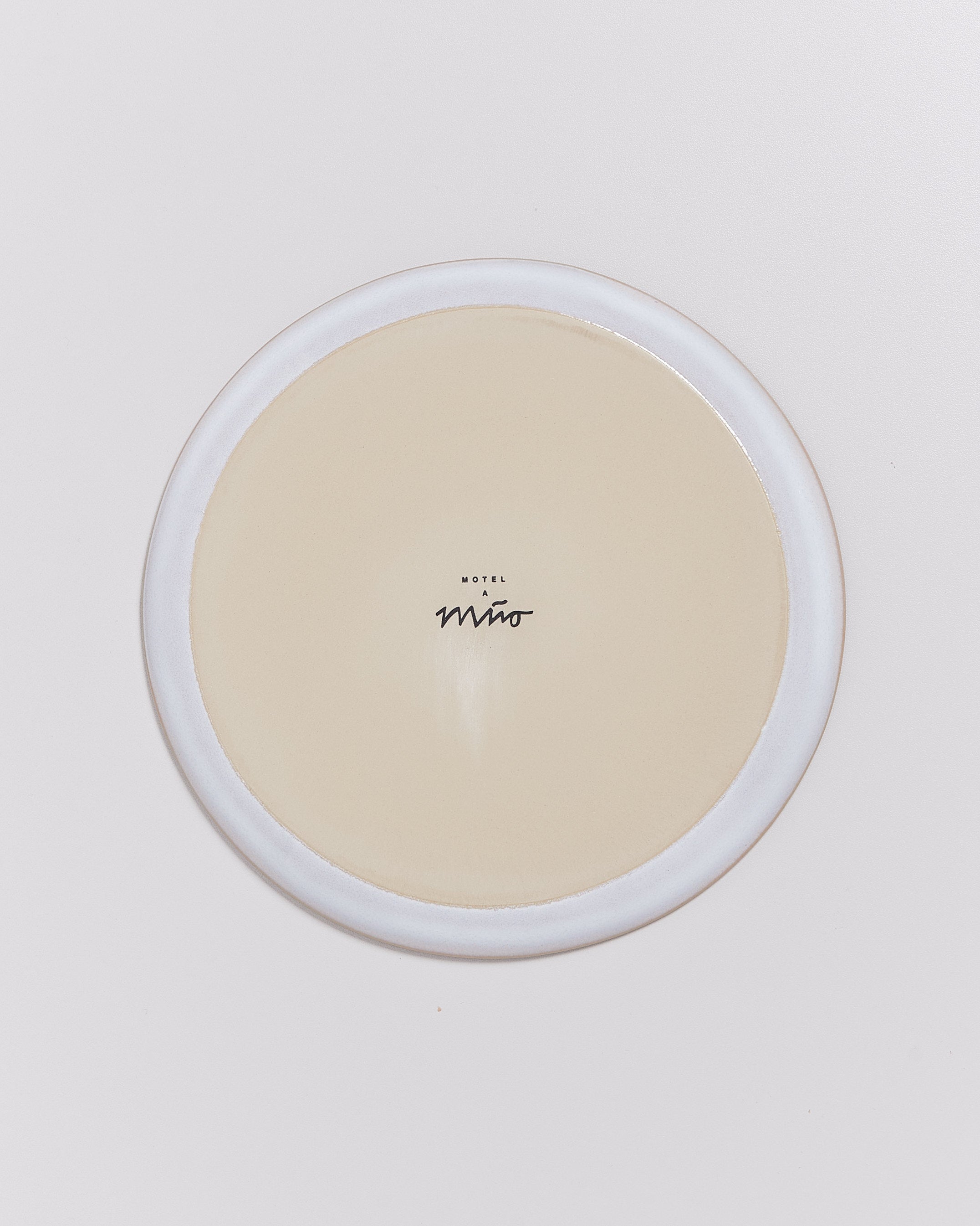 Ein runder, beigefarbener Teller mit der Aufschrift "Motel a Miio" in der Mitte auf weißem Hintergrund.