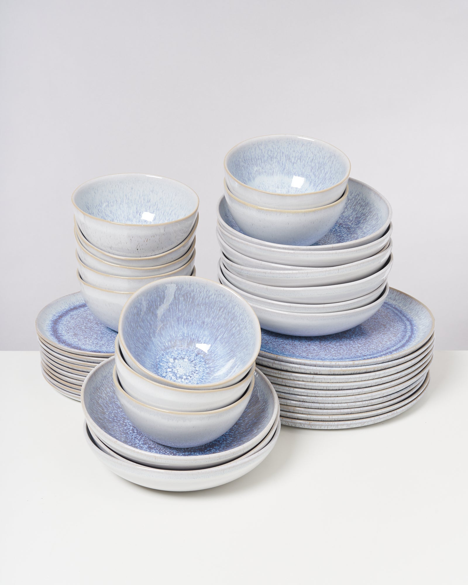 Gestapelte, blaue Keramikschüsseln und -teller stehen auf einem Tisch vor neutralem Hintergrund.