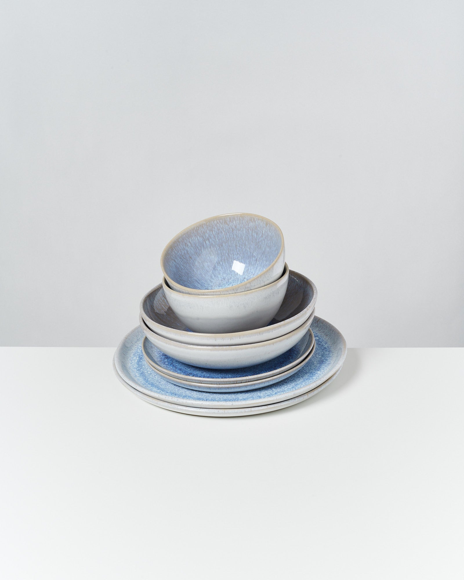 Ein Stapel aus zwei blauen Schalen und zwei Tellern auf einem weißen Tisch.