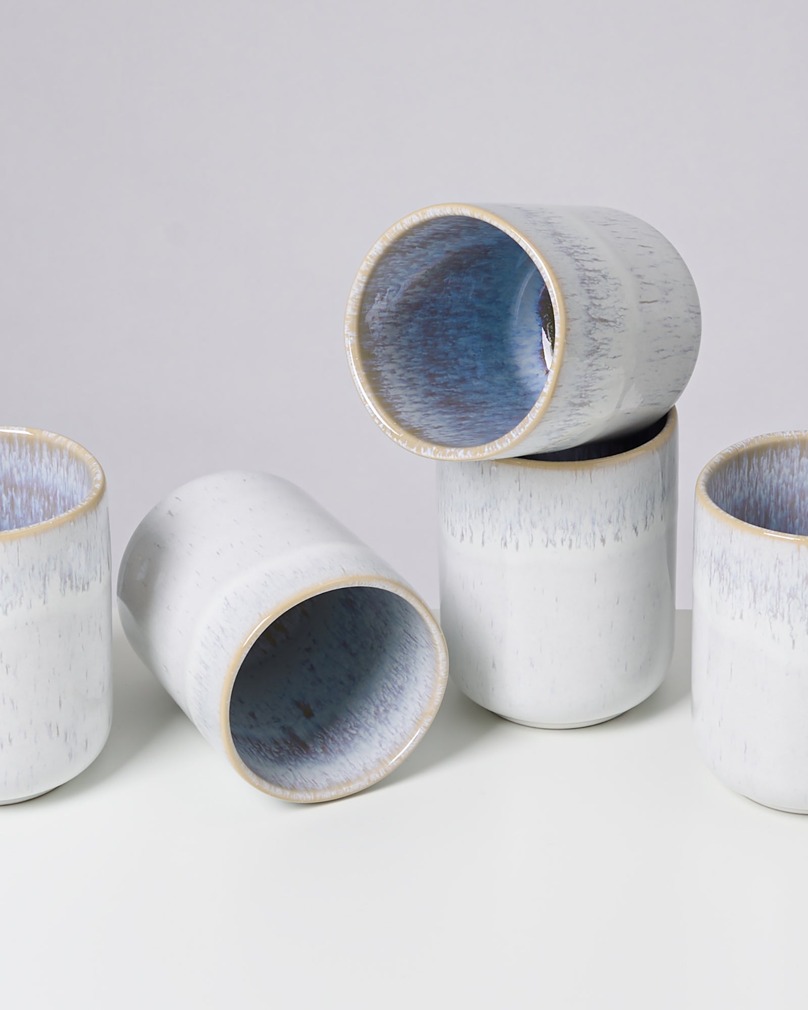 Fünf weiße Keramiktassen mit blauer Innenseite, teilweise liegend und gestapelt.