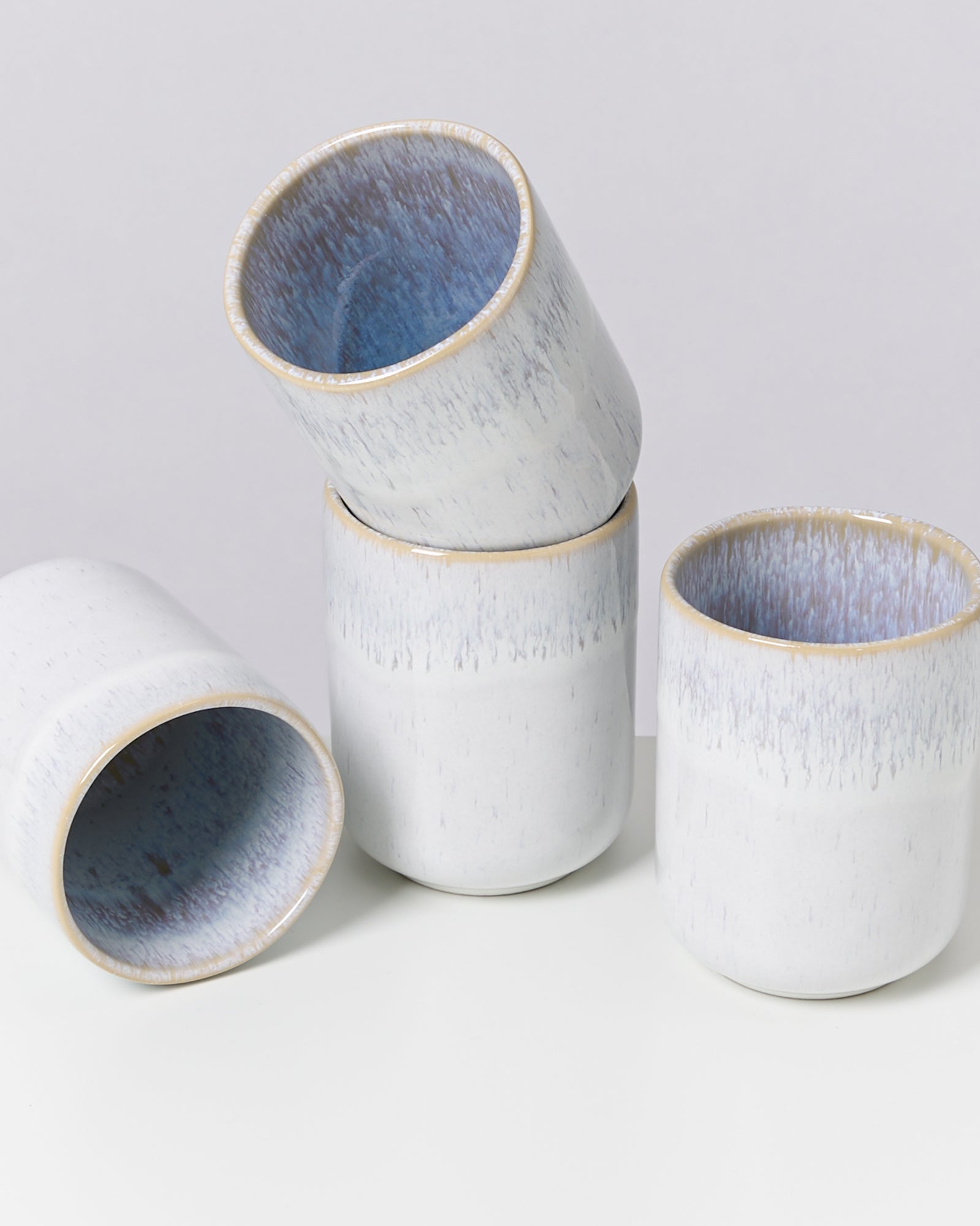 Vier hellblaue Keramikbecher stehen auf einem Tisch, einer liegt seitlich.