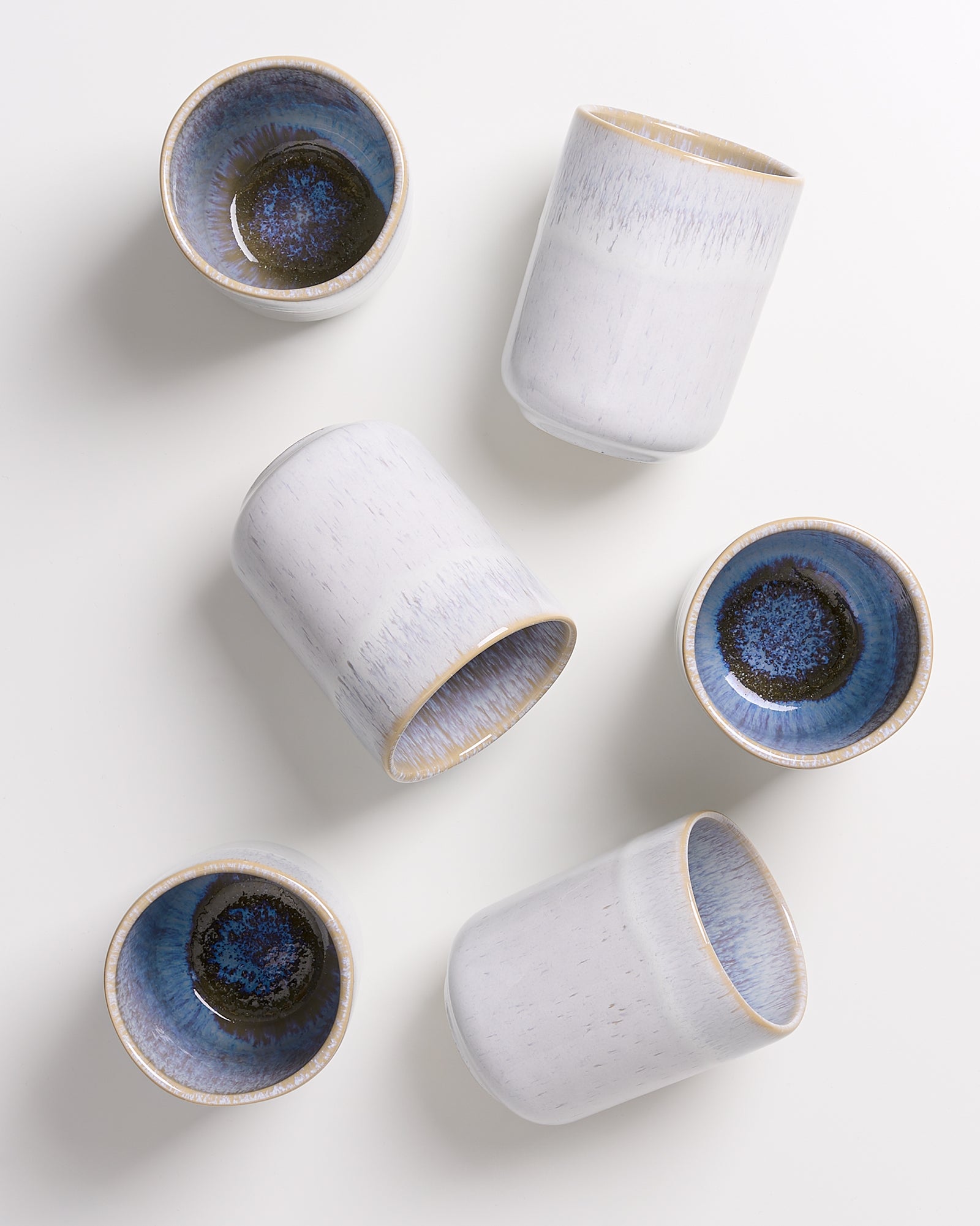 Sechs weiße Keramikbecher mit blauen Innenseiten liegen auf einem weißen Hintergrund.