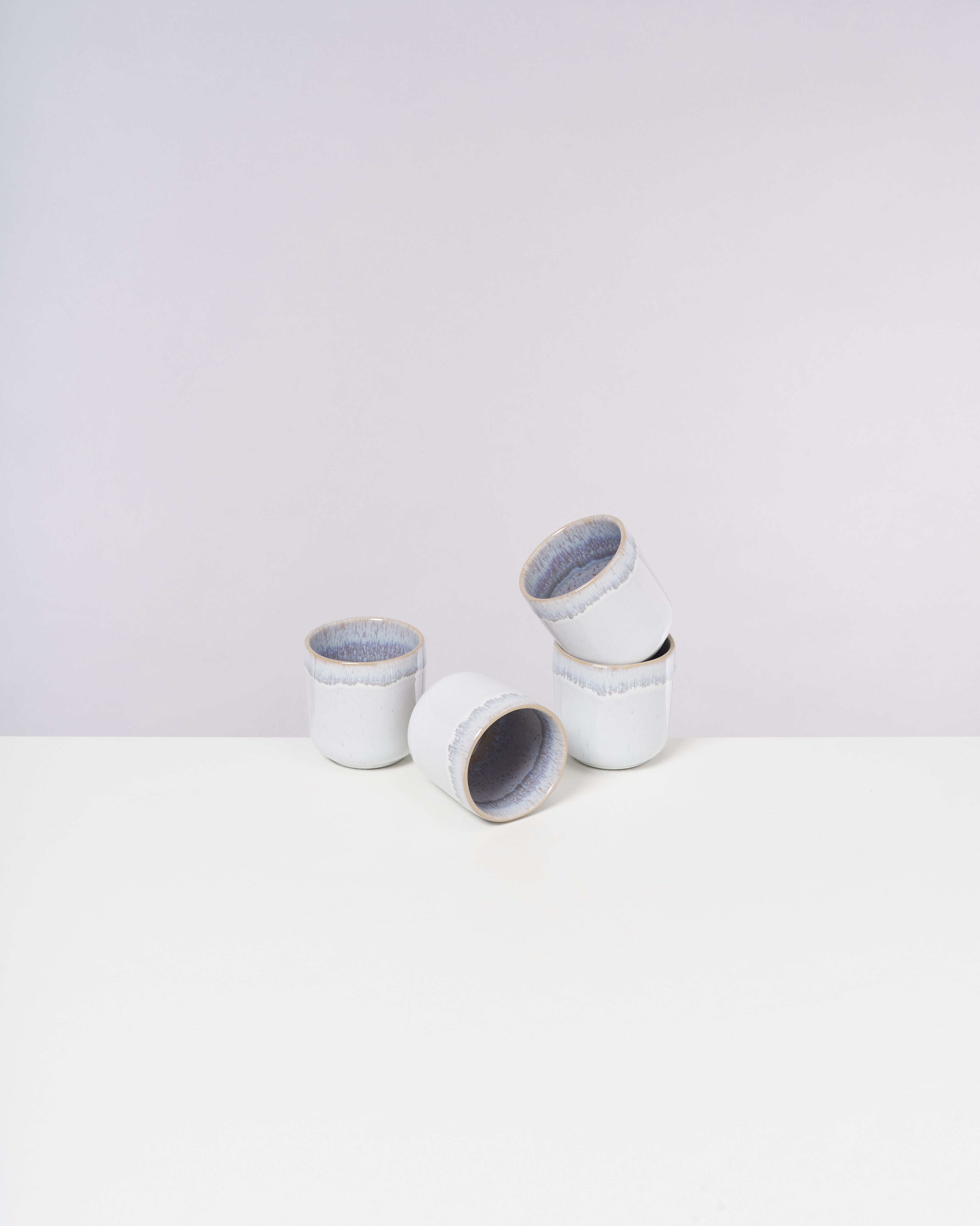 Vier weiße Keramiktassen mit blauer Innenseite auf einem weißen Hintergrund, eine liegt seitlich.