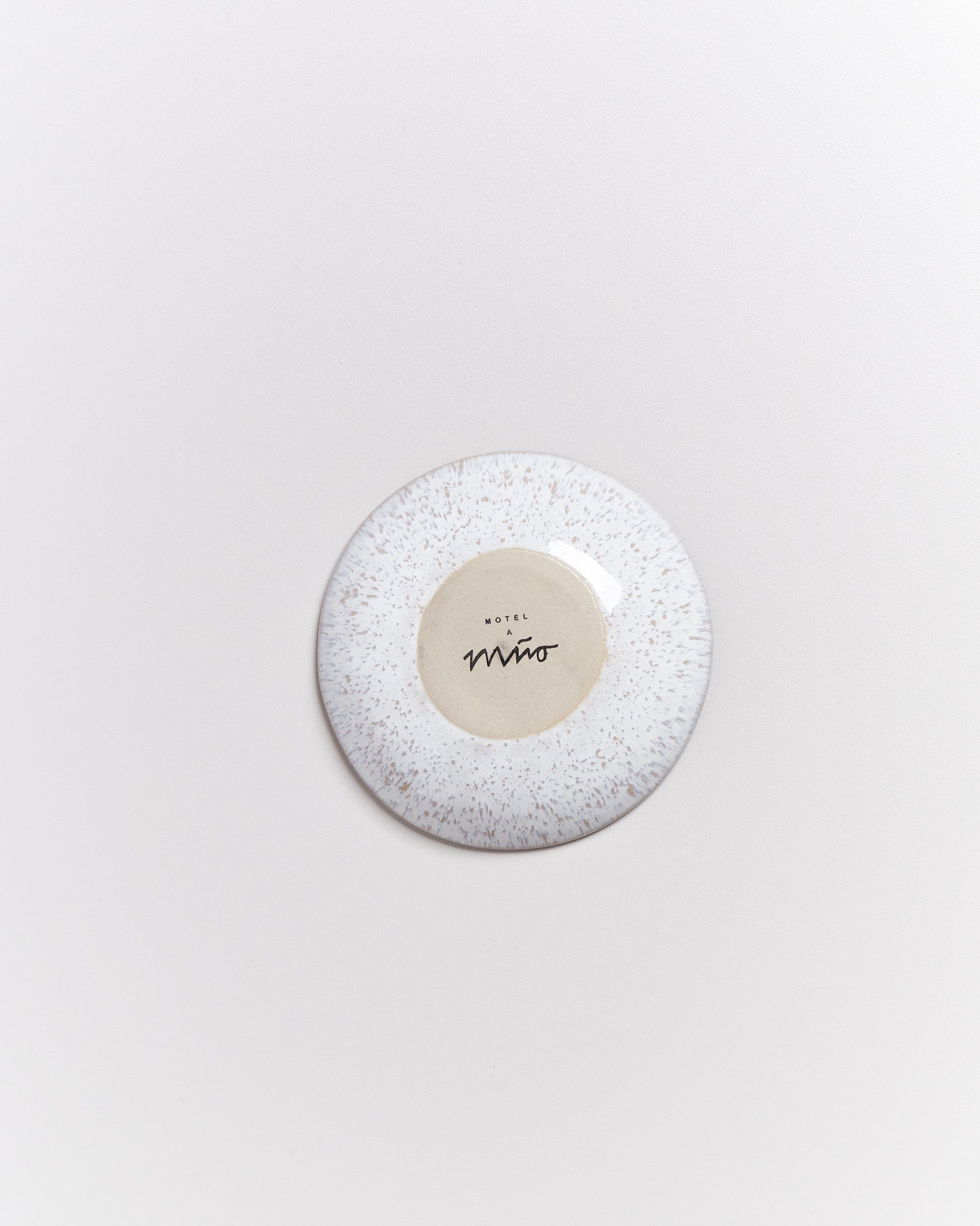 Runder Teller mit fleckigem Muster und Hotel-Memo-Markierung auf hellem Hintergrund.