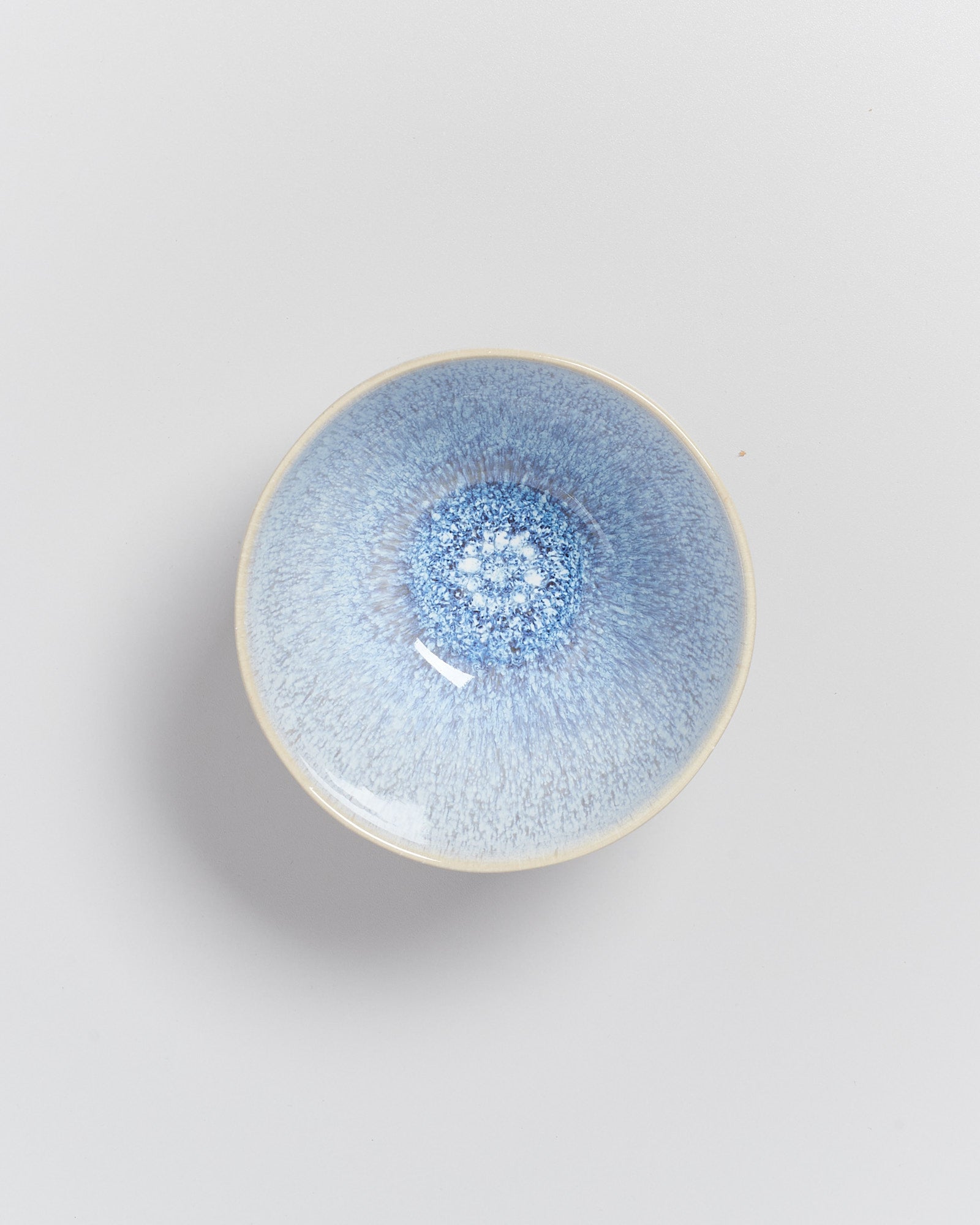 Blaue Keramikschale mit einem faszinierenden, körnigen Muster, das von der Mitte nach außen ausstrahlt, auf grauem Hintergrund.