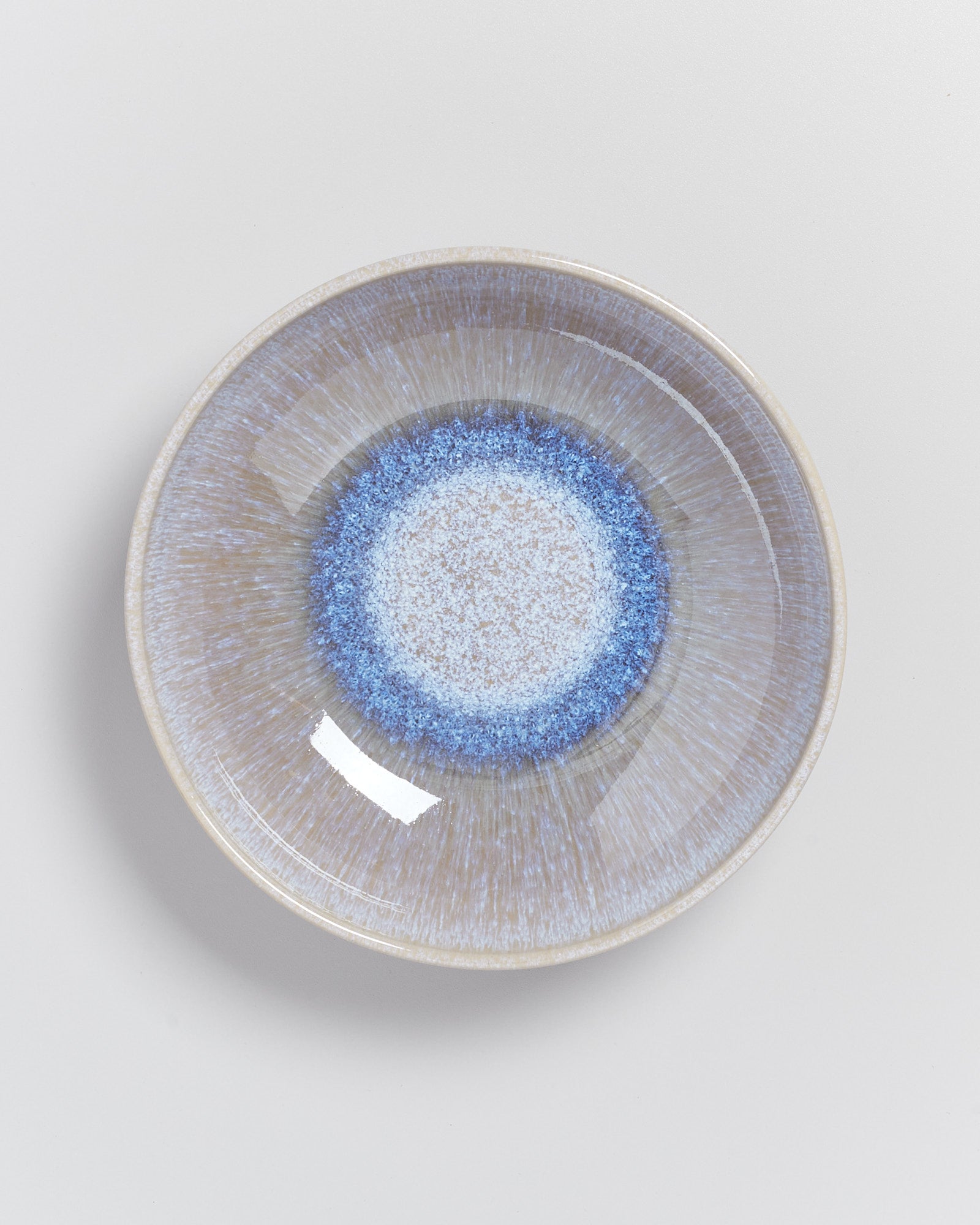 Keramikschale mit blau-weißer Glasur im Zentrum und radialer Musterung auf hellem Hintergrund.