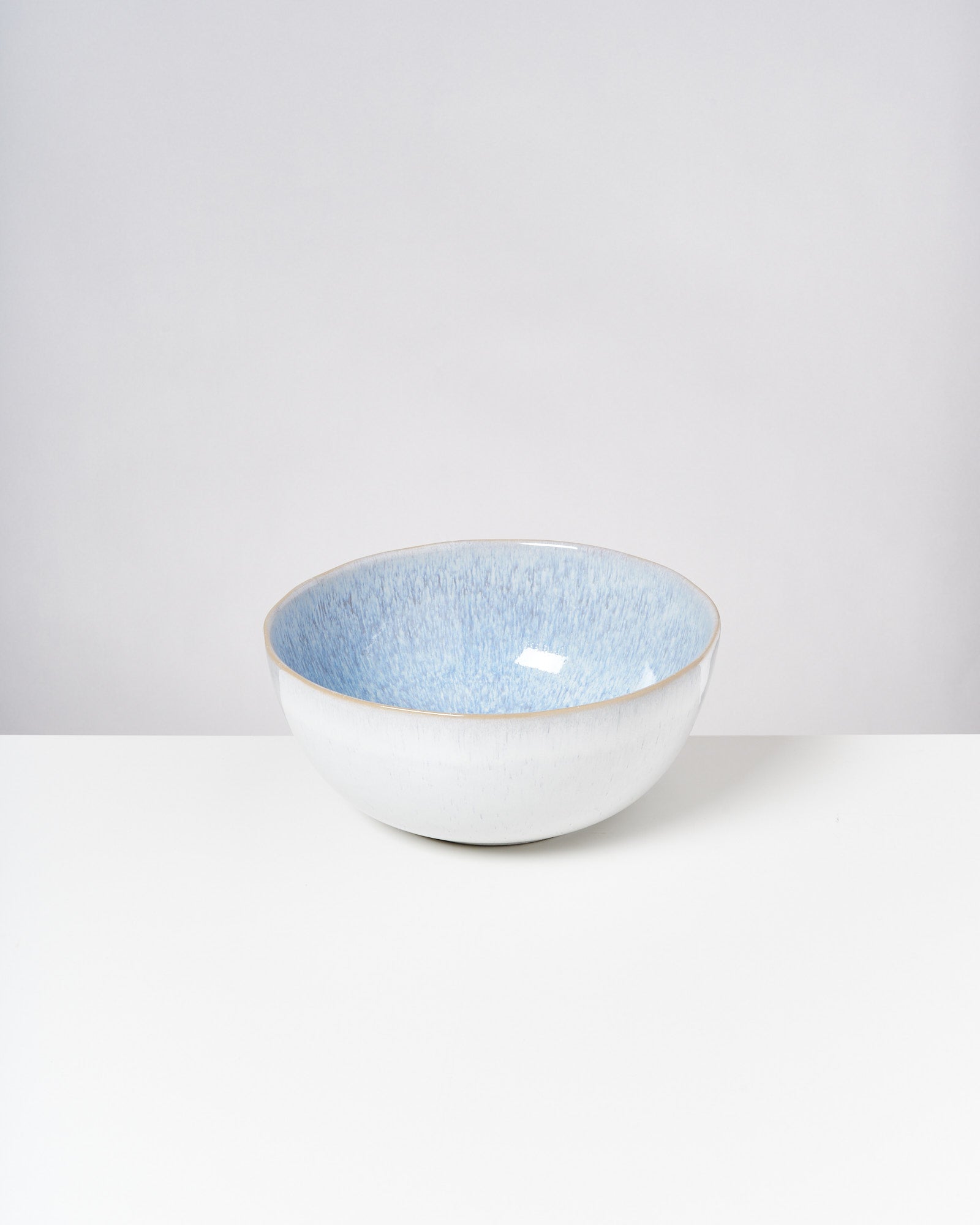 Eine weiße Schüssel mit hellblauer Innenseite steht auf einem weißen Tisch vor neutralem Hintergrund.