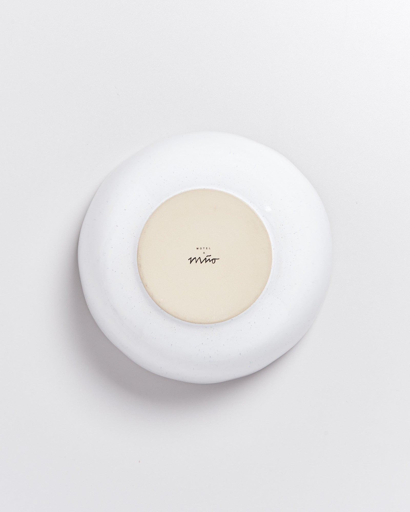 Weiße, runde Keramikschale mit cremefarbener Mitte und der Aufschrift "Hotel Miro" auf der Unterseite auf weißem Hintergrund.