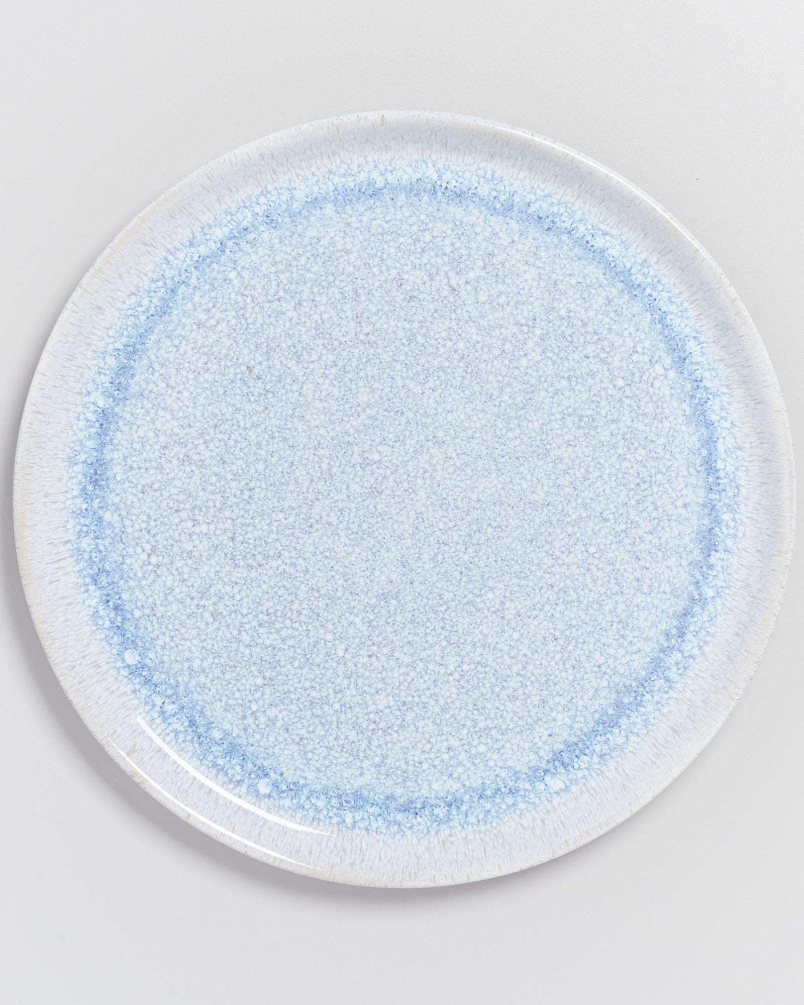 Ein runder, hellblauer Keramikteller mit feiner, gesprenkelter Oberfläche auf einem weißen Hintergrund.