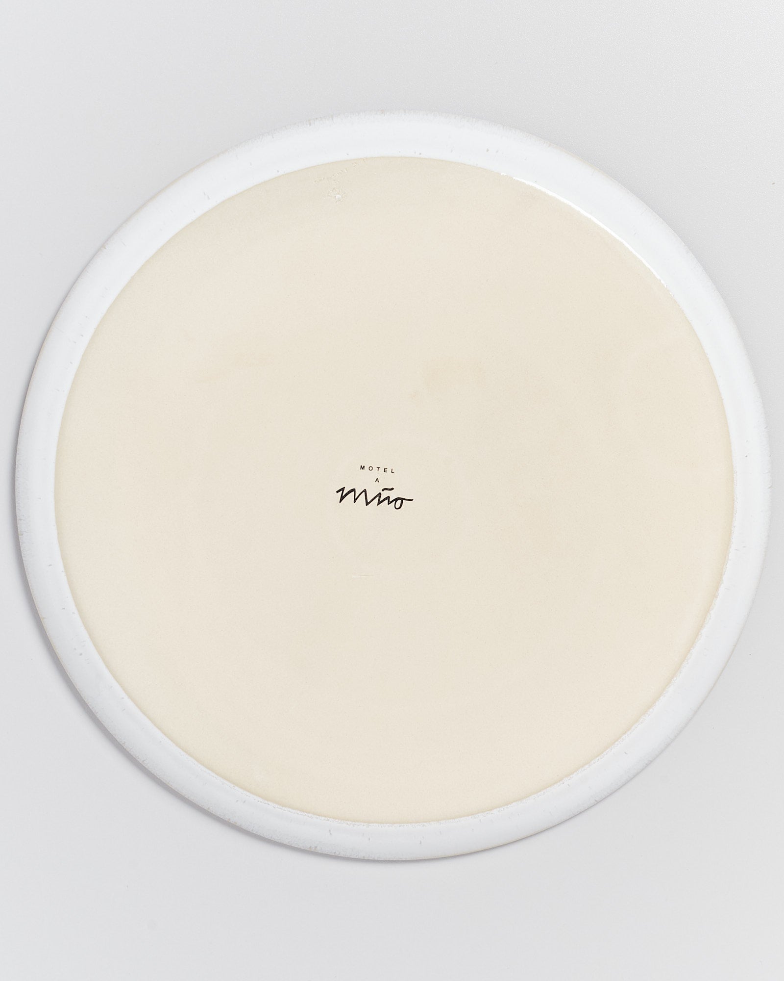 Unterseite eines runden Tellers mit einem Logo in der Mitte auf hellem Hintergrund.