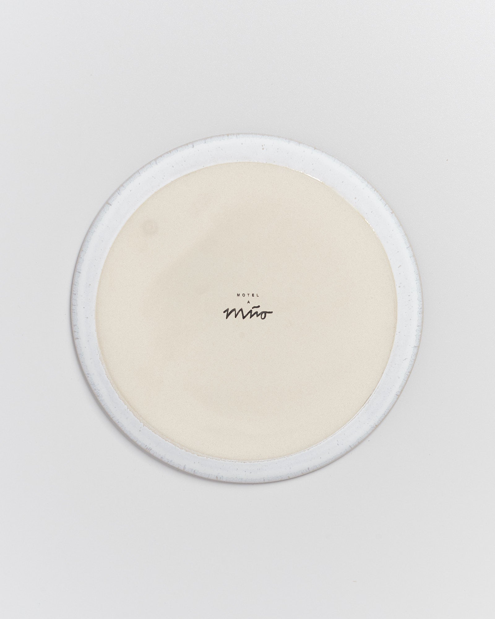 Rundes, helles Keramikobjekt mit der Aufschrift "Motel a Miro" in der Mitte auf einem weißen Hintergrund.