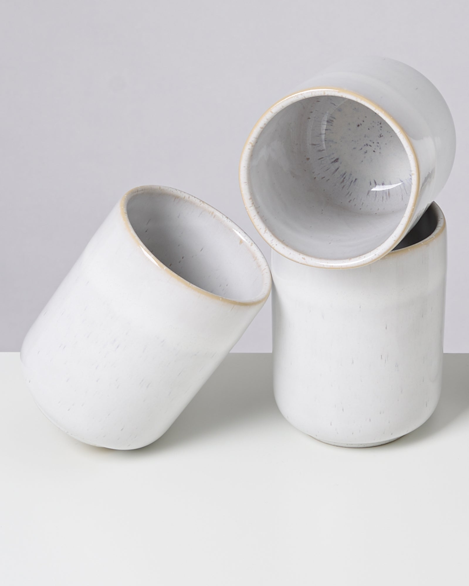 Drei weiße Keramiktassen, die aufeinander gestapelt sind, auf einem weißen Untergrund.