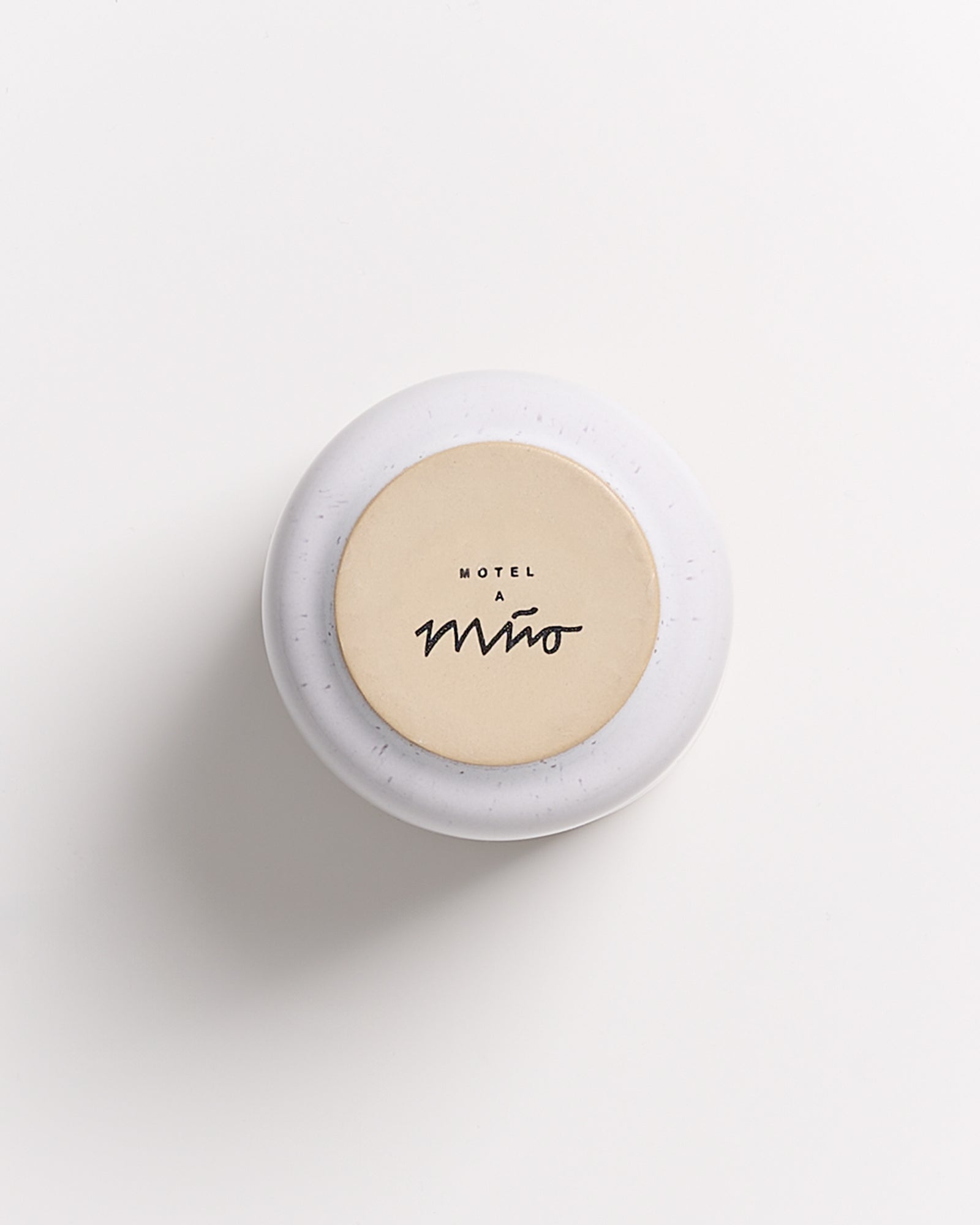 Runder, weißer Behälter mit beigem Deckel, auf dem "Motel a Miio" steht, auf weißem Hintergrund.