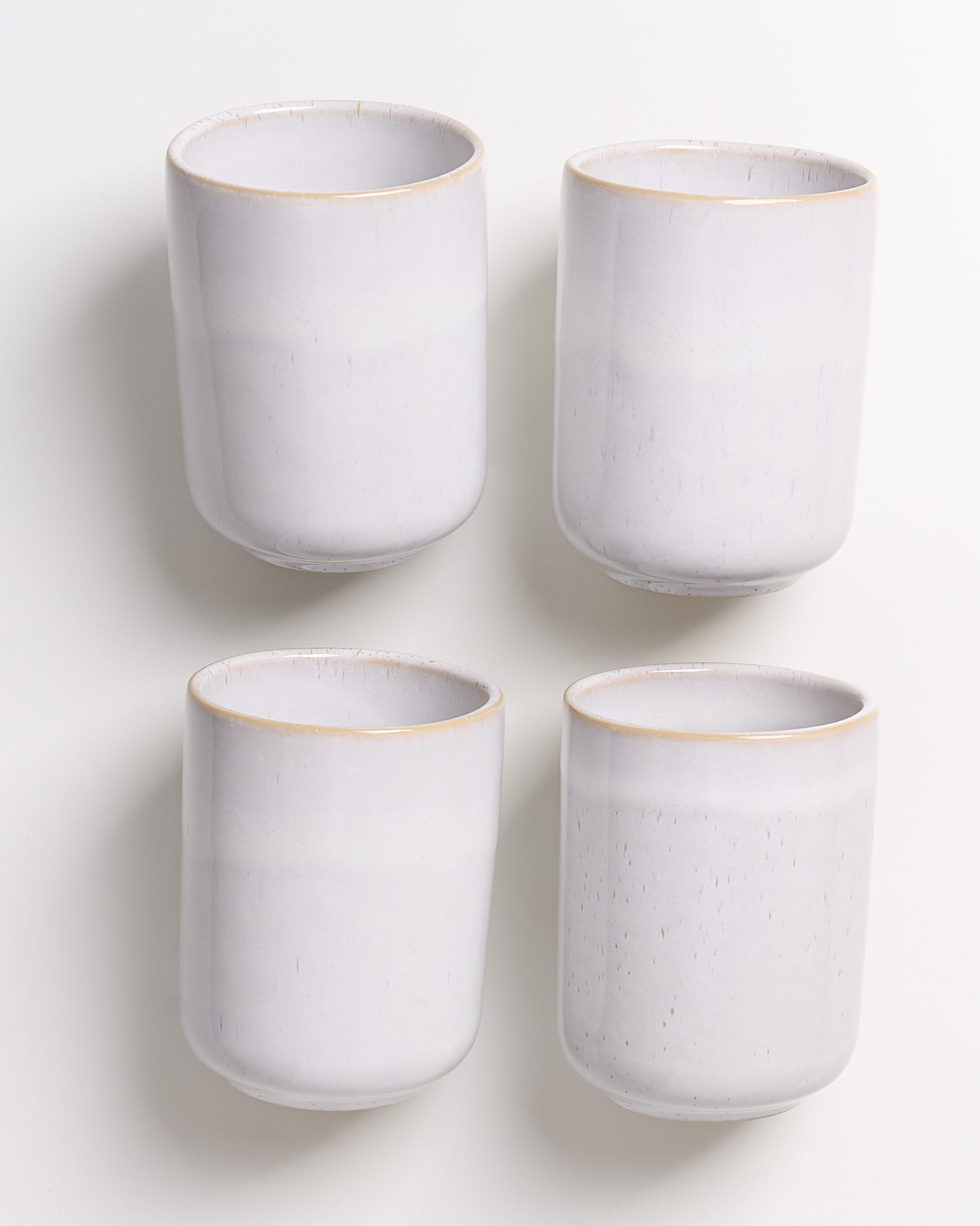 Vier weiße Keramiktassen mit leicht bräunlichem Rand vor einem weißen Hintergrund.