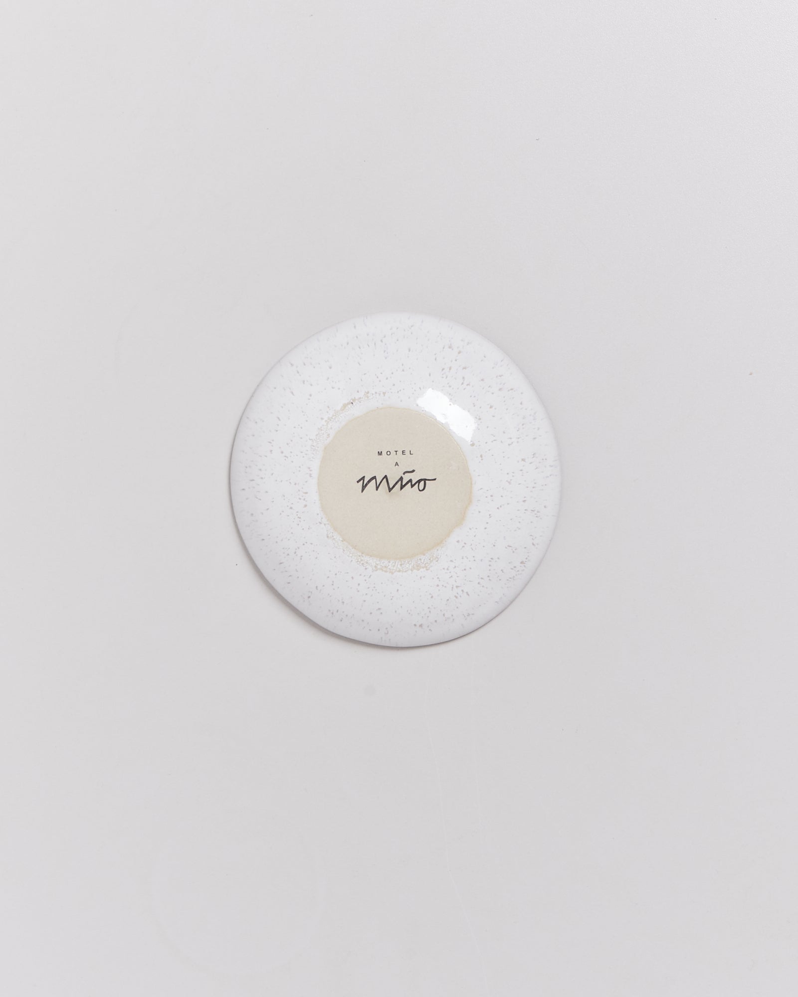 Weiße Untertasse mit dem Schriftzug "Motel Miro" auf einem hellen Hintergrund.