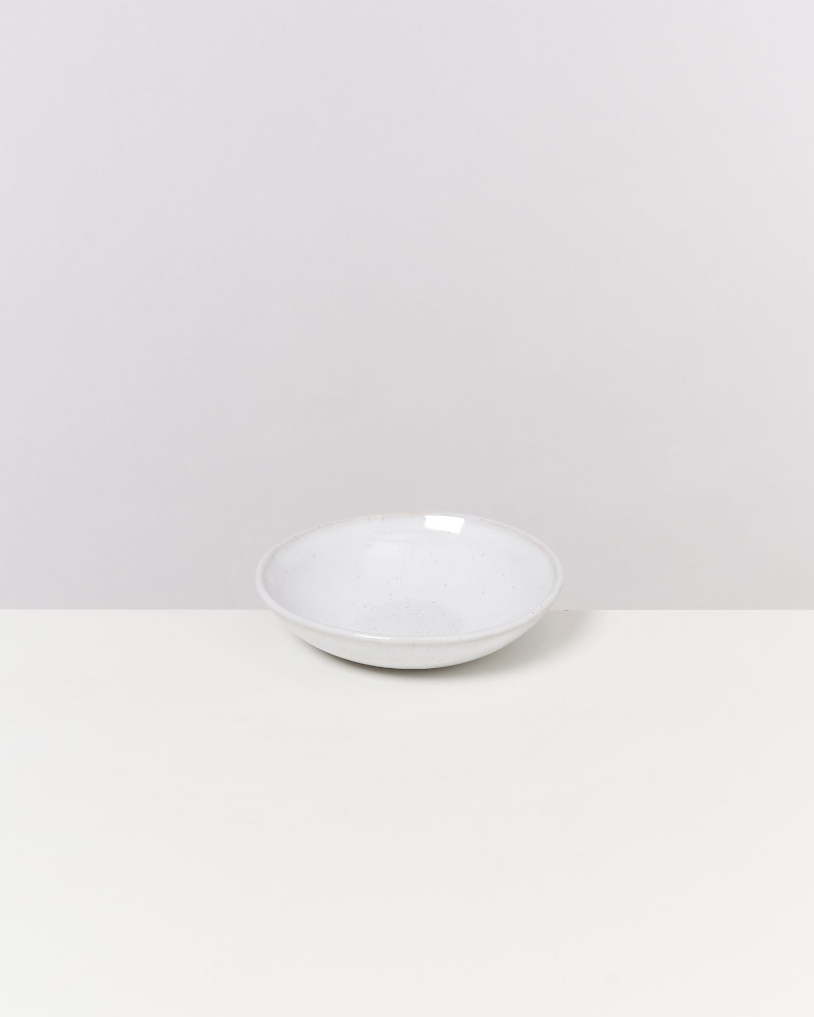 Eine weiße, flache Schale steht auf einem weißen Tisch vor einem hellgrauen Hintergrund.