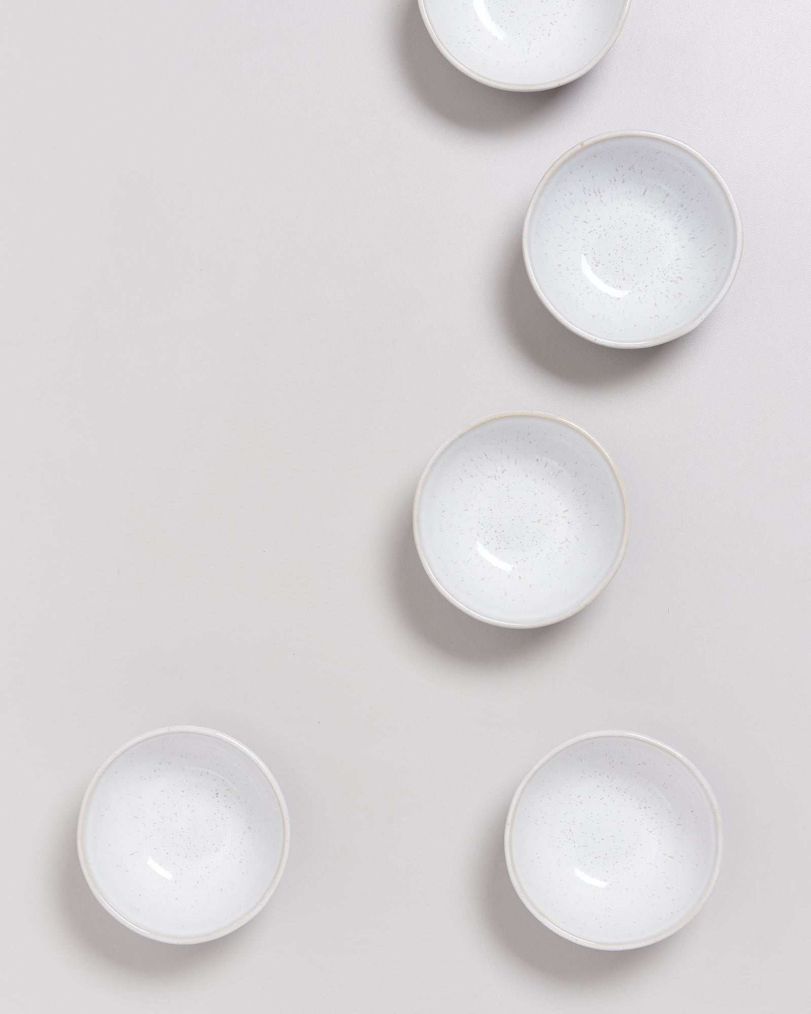 Fünf weiße, runde Schalen liegen auf einer hellgrauen Oberfläche in einer diagonalen Anordnung.