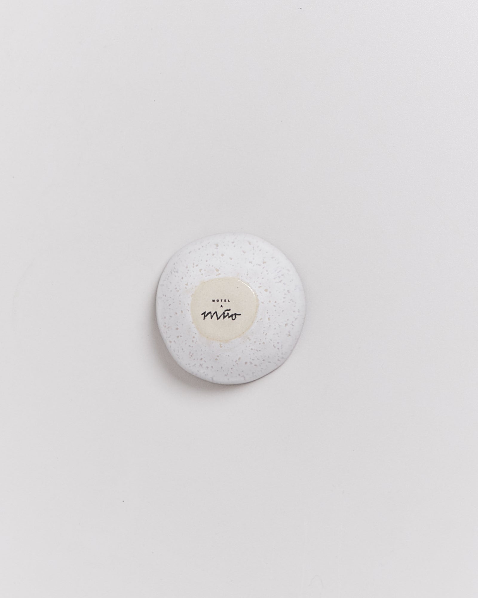 Weißes, rundes Objekt mit Etikett "Hotel Miro" auf hellem Hintergrund.