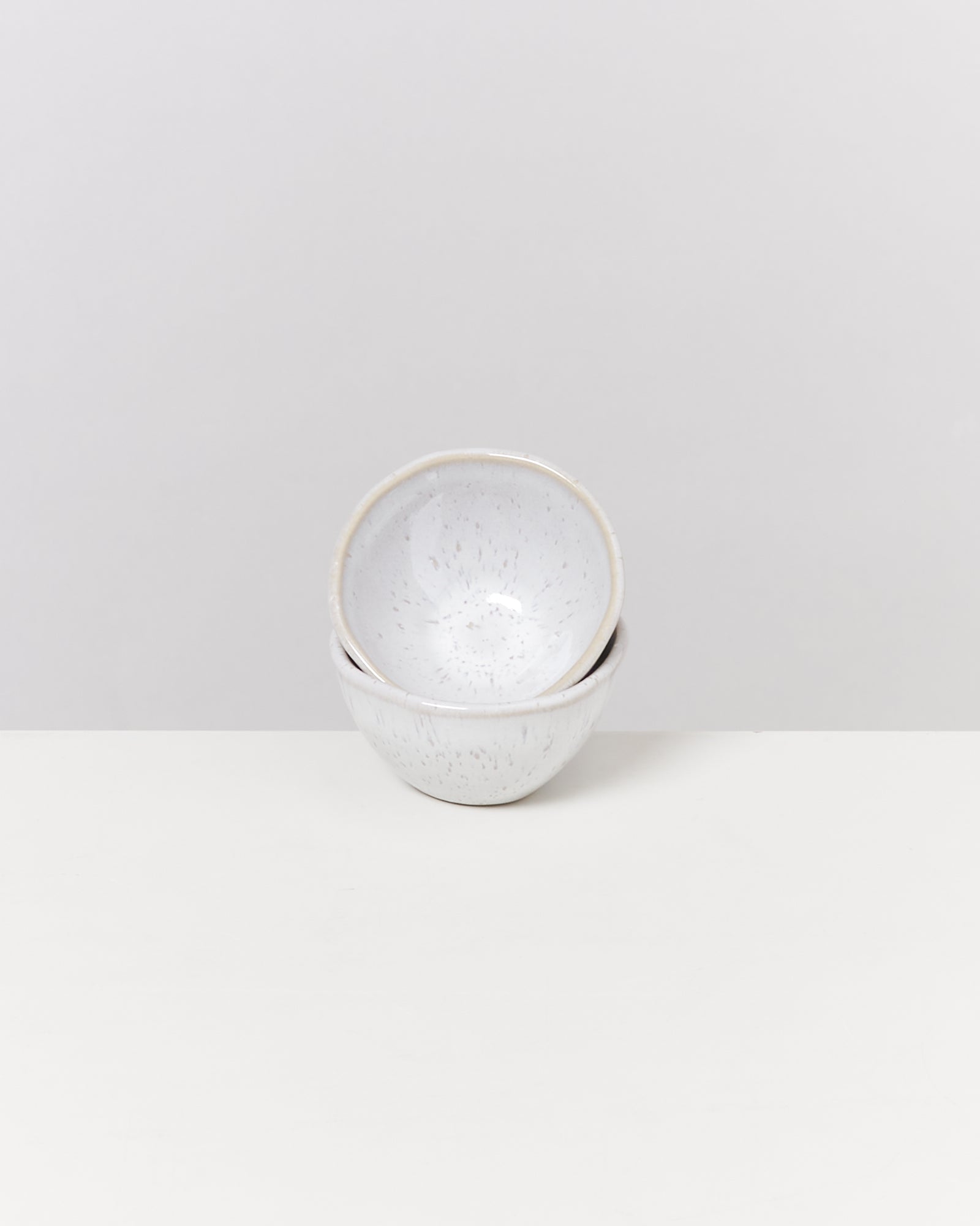 Zwei gestapelte, weiß gesprenkelte Keramikschalen auf einem weißen Hintergrund.