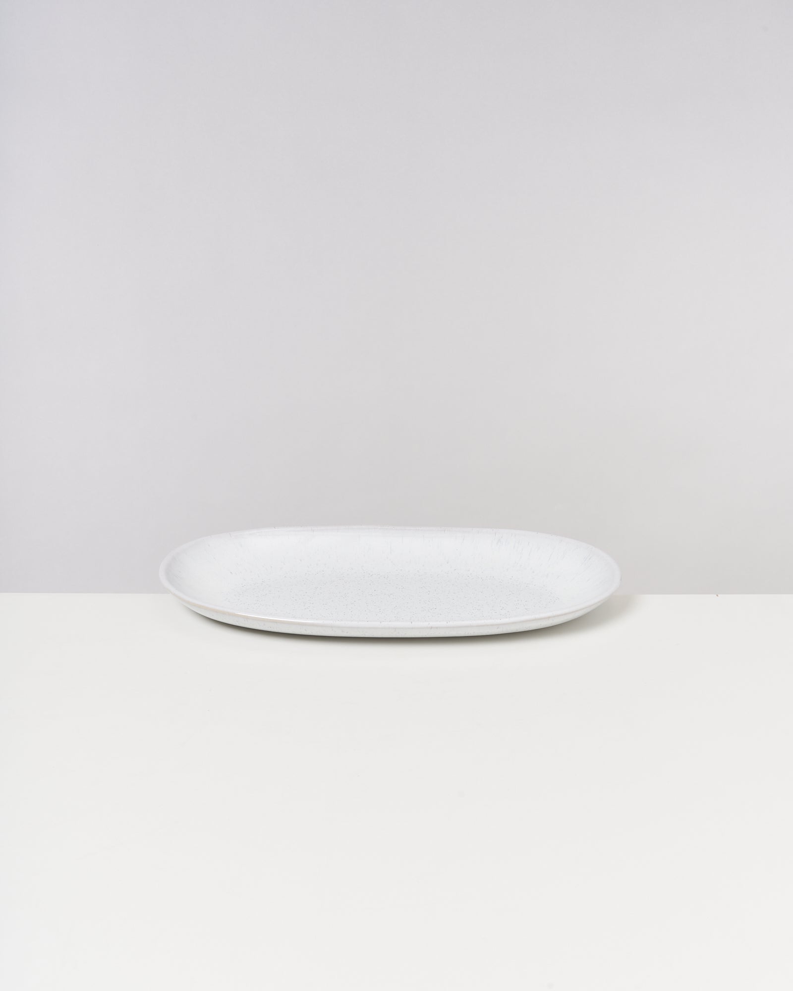 Ein weißer, runder Teller steht auf einer weißen Oberfläche vor einem neutralen Hintergrund.