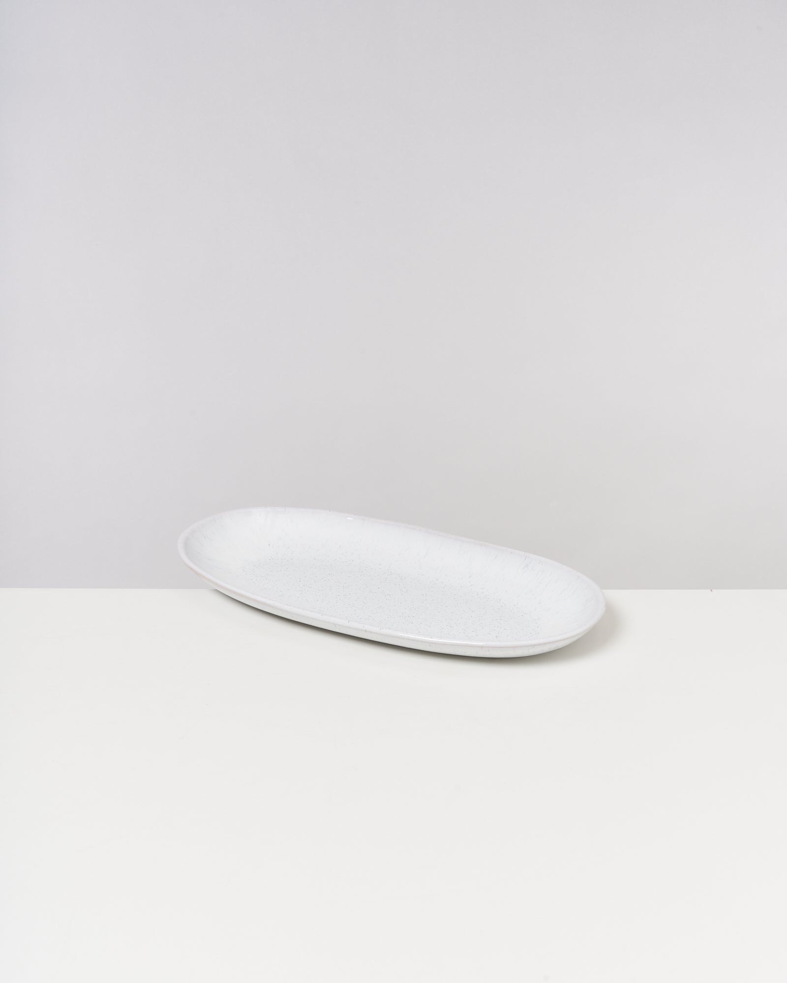 Ovaler, weißer Teller auf einem weißen Tisch vor grauem Hintergrund.
