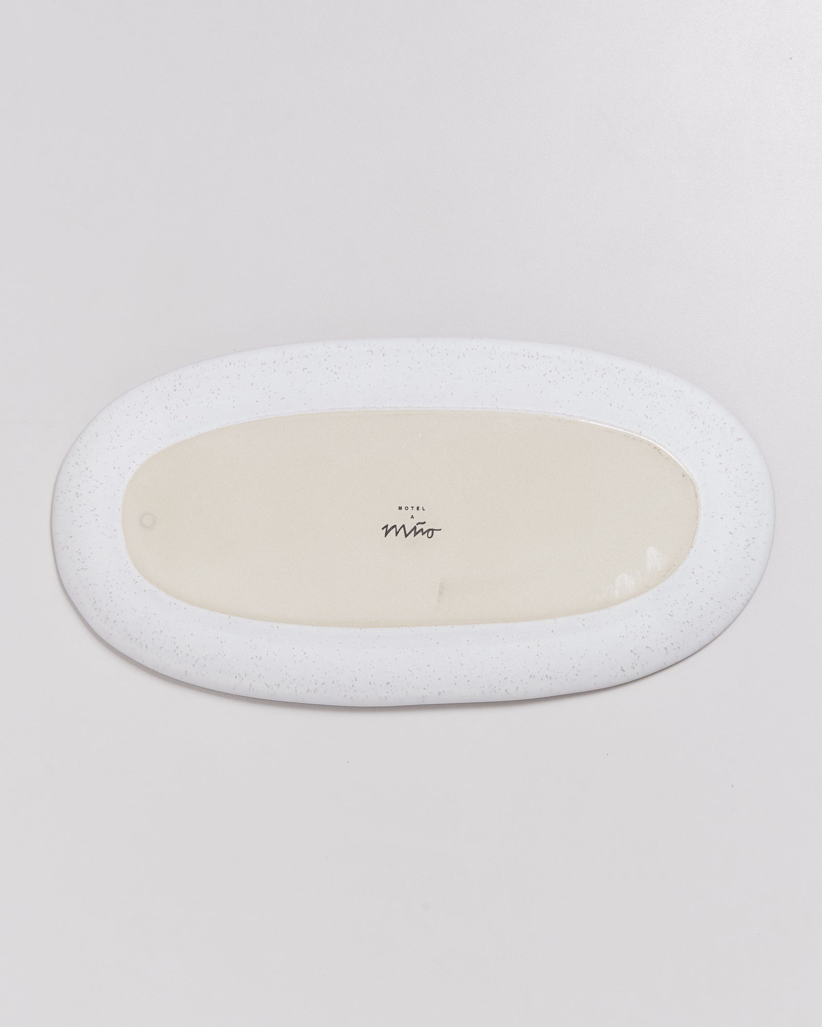 Ovaler, flacher keramischer Teller mit weißem Rand und beiger Mitte auf hellem Hintergrund.