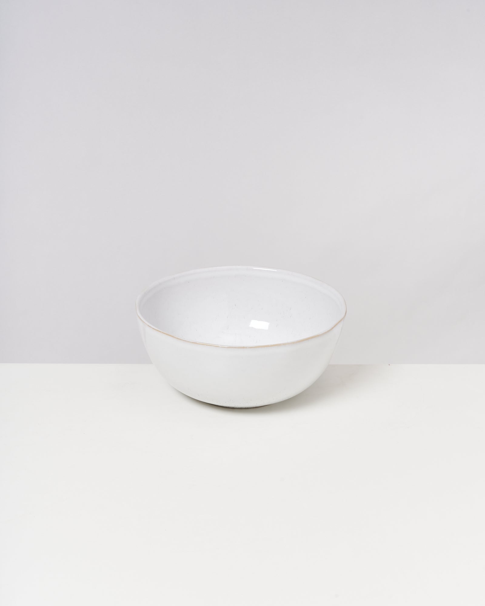 Eine einfache weiße Schüssel steht auf einem weißen Tisch vor einem grauen Hintergrund.