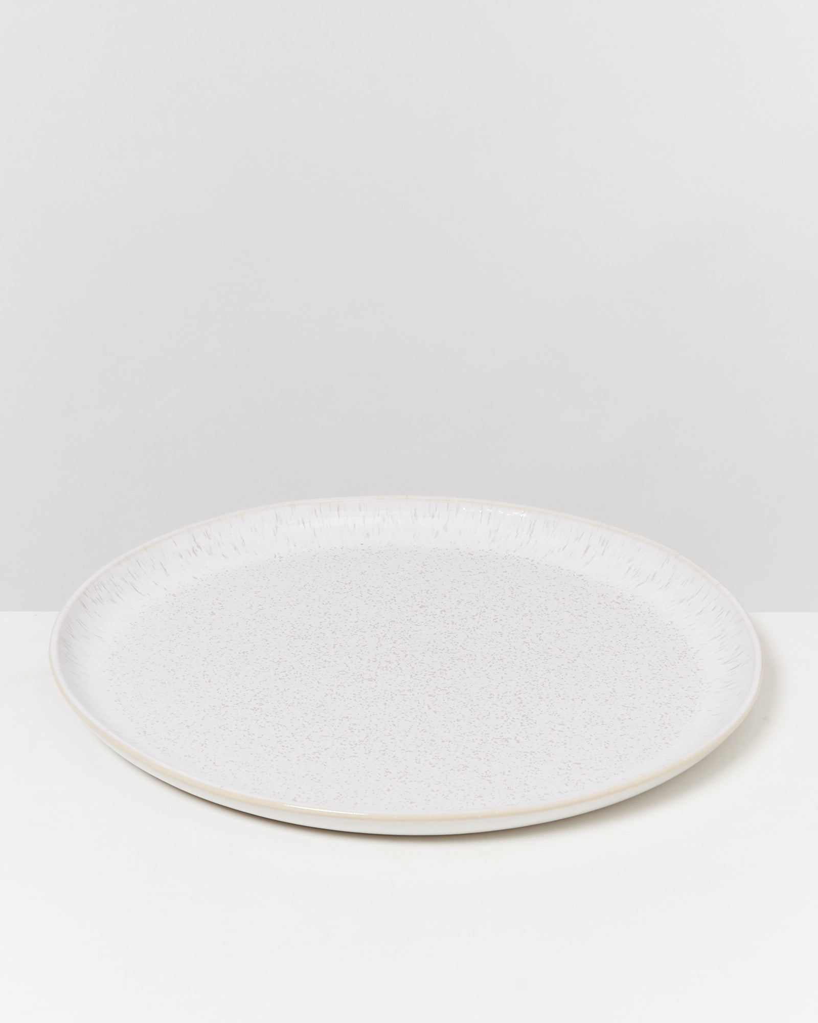 Weiße runde Keramikplatte mit feiner Textur auf einer weißen Oberfläche vor grauem Hintergrund.