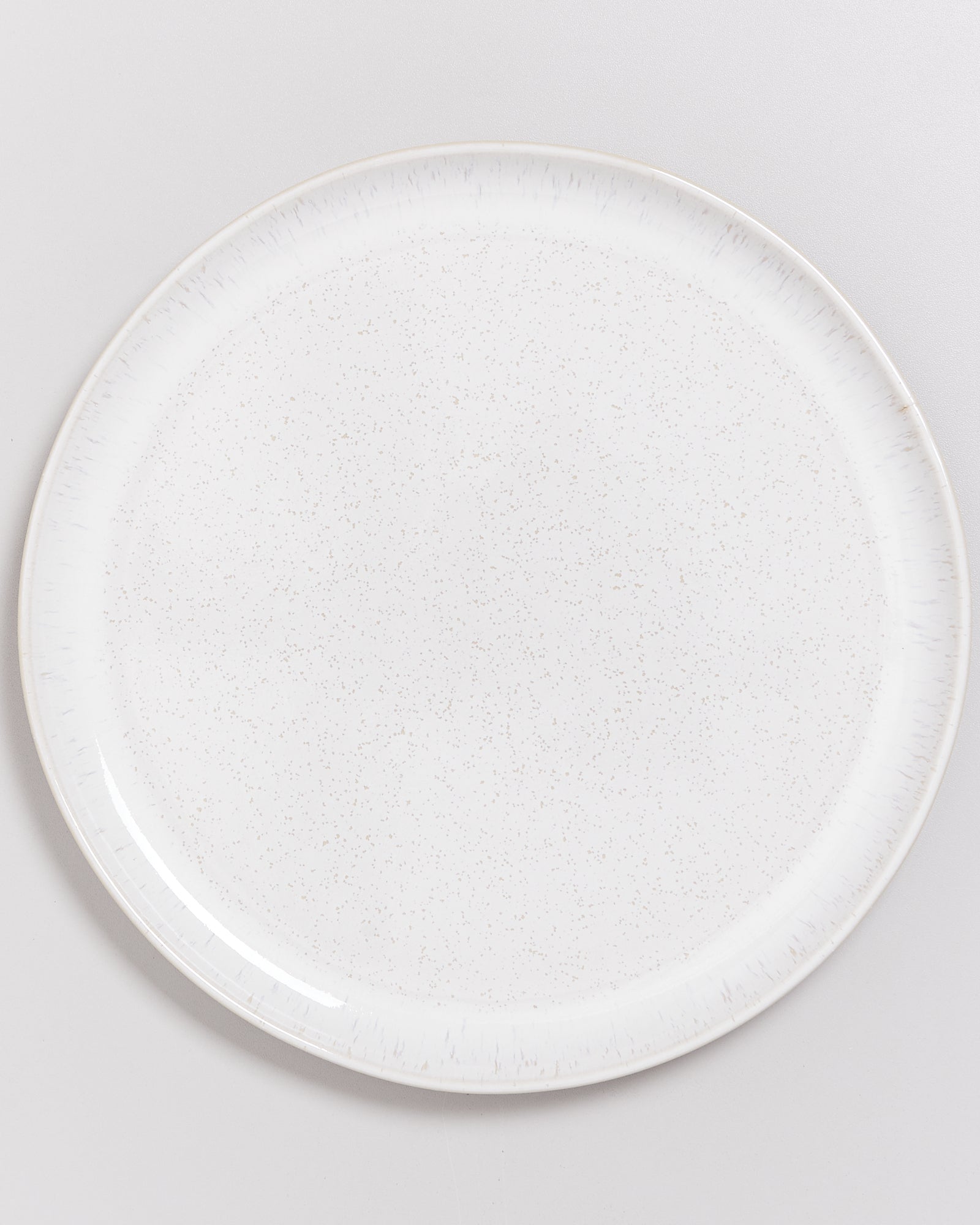 Weißer, runder Teller mit einem dezenten gesprenkelten Muster auf weißem Hintergrund.
