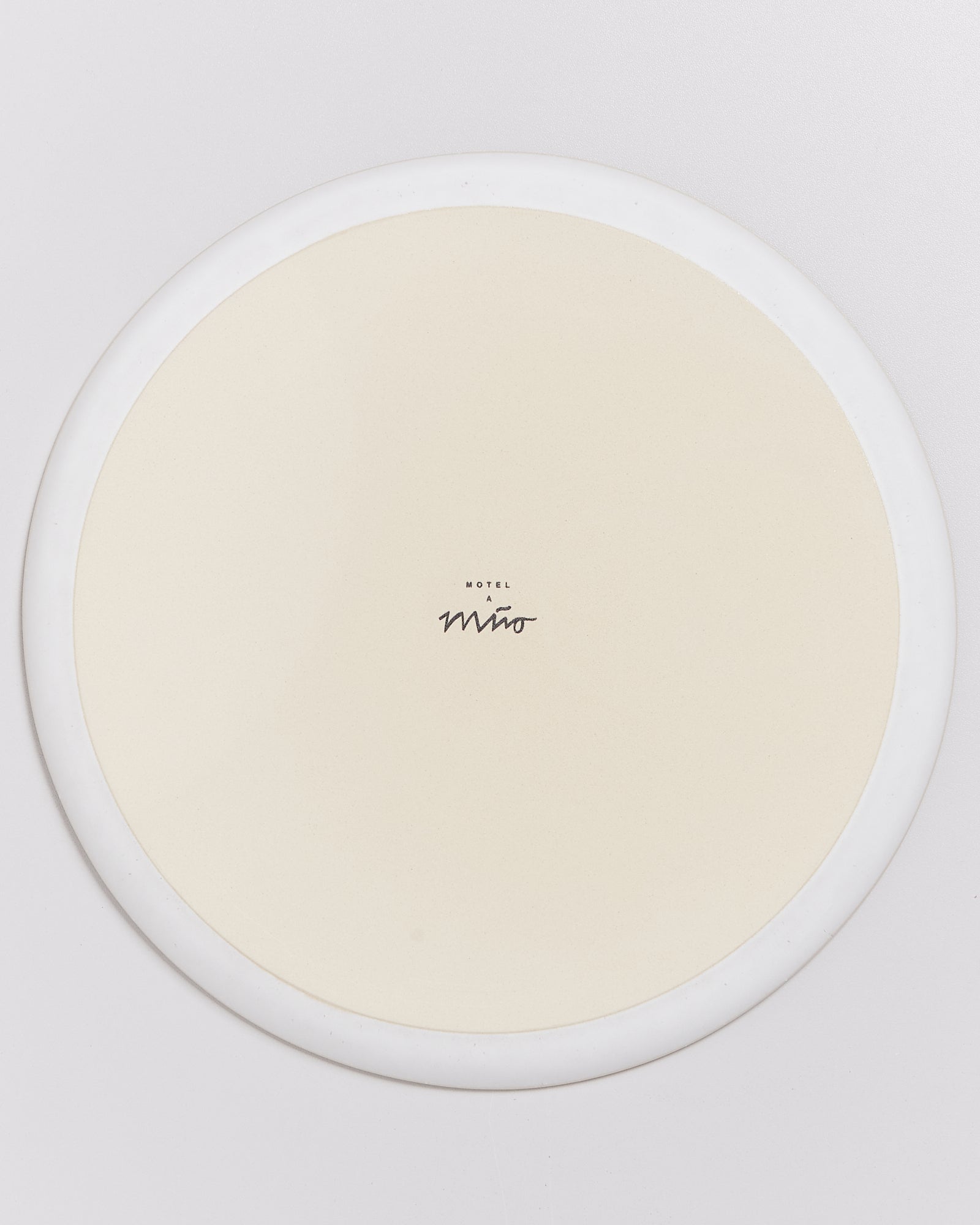 Ein runder, beiger Teller mit weißem Rand und der Aufschrift "Motel a Miro" in der Mitte.