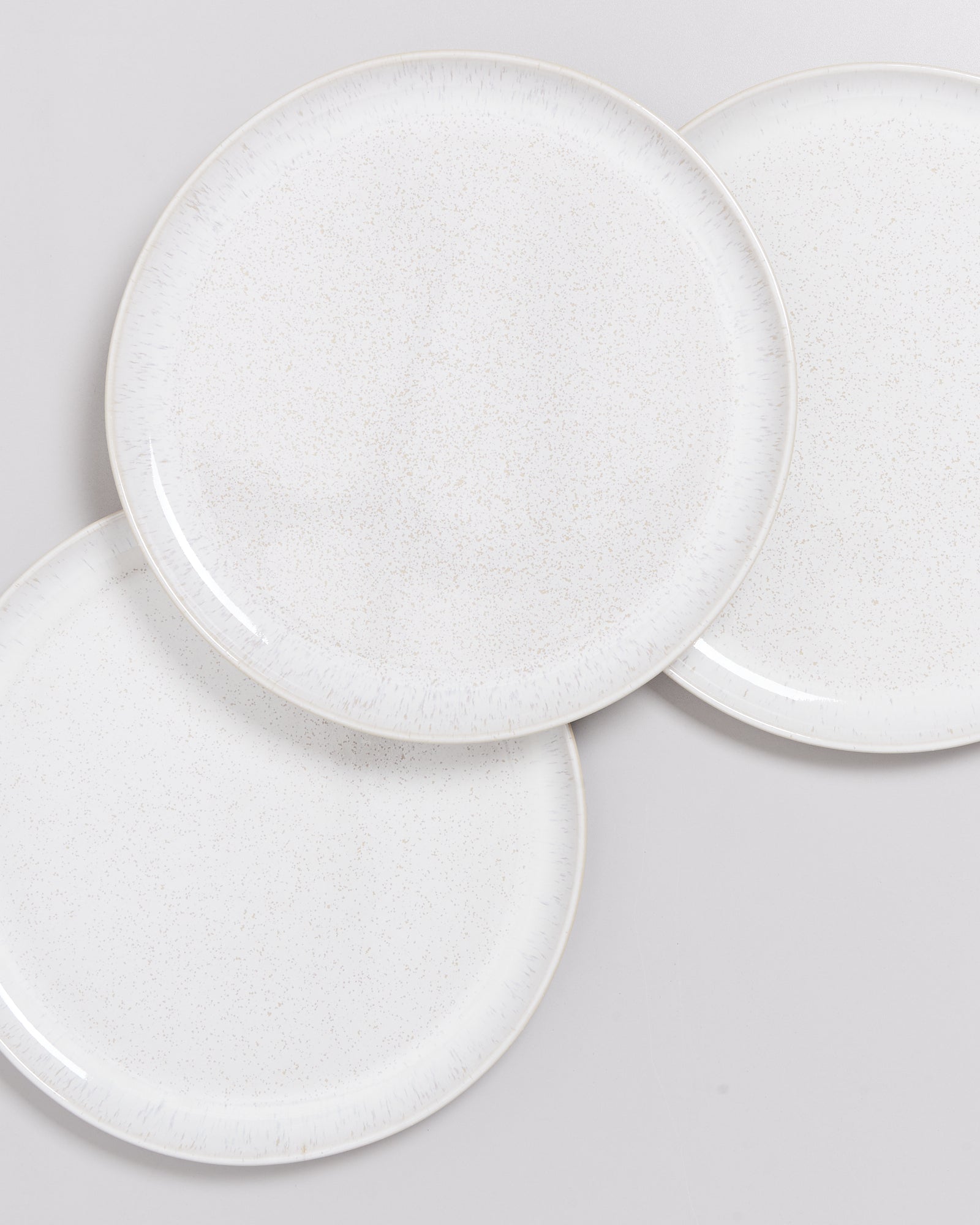 Drei überlappende weiße Teller mit feiner Sprenkelung auf grauem Hintergrund.
