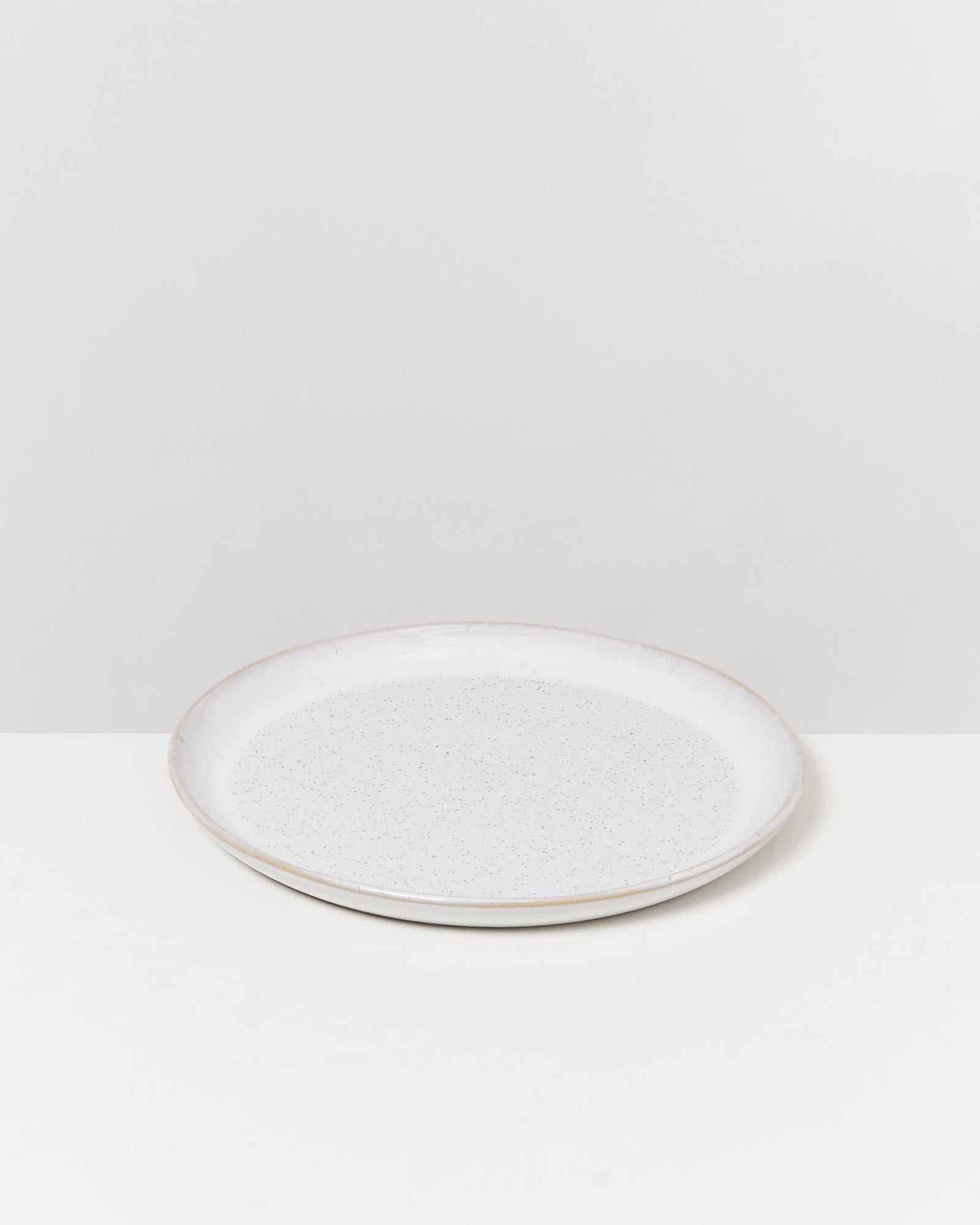 Weißer, runder Teller mit leicht glänzender Oberfläche auf hellgrauem Hintergrund.