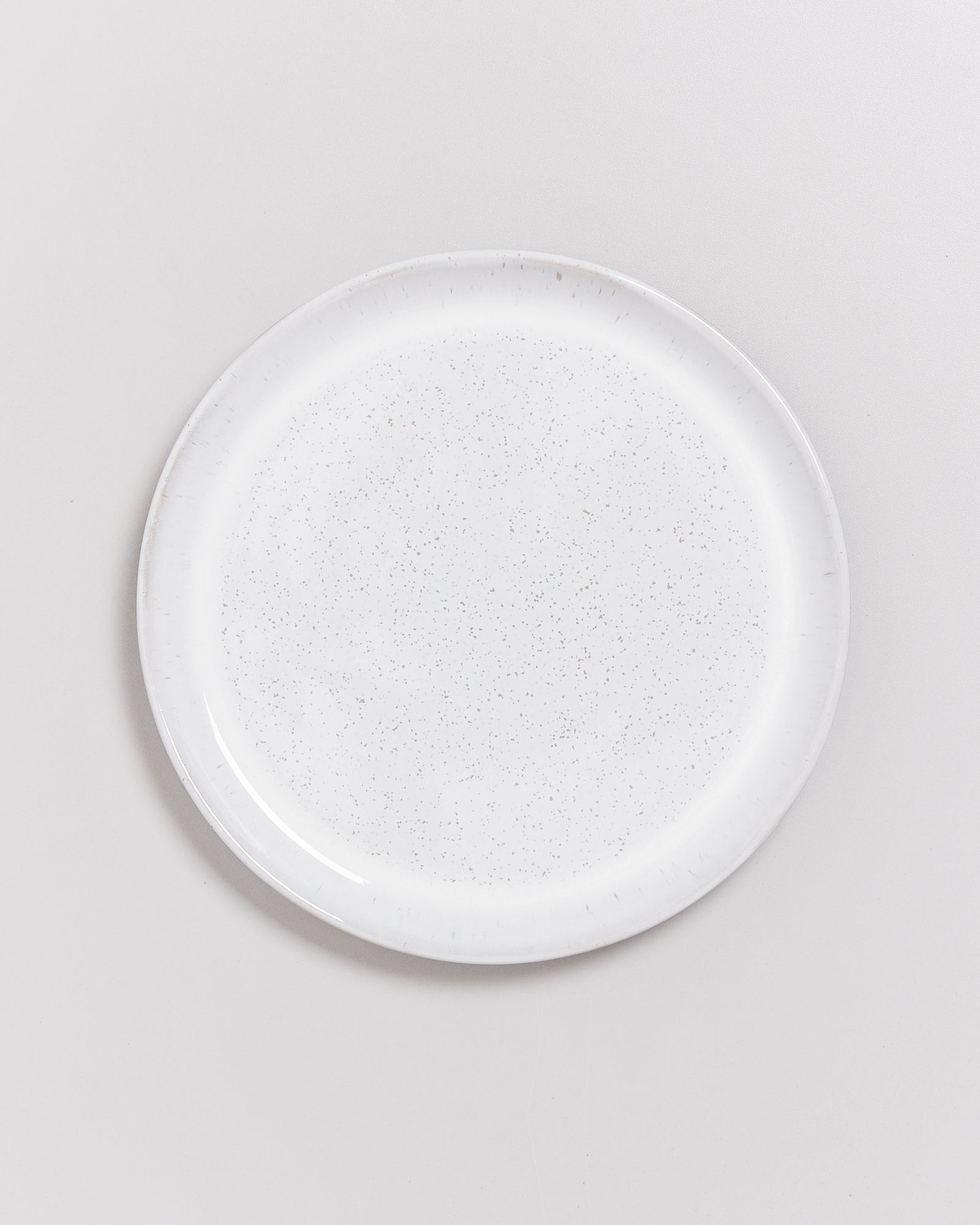 Weißer, runder Teller mit leichtem Sprenkelmuster, vor neutralem Hintergrund.