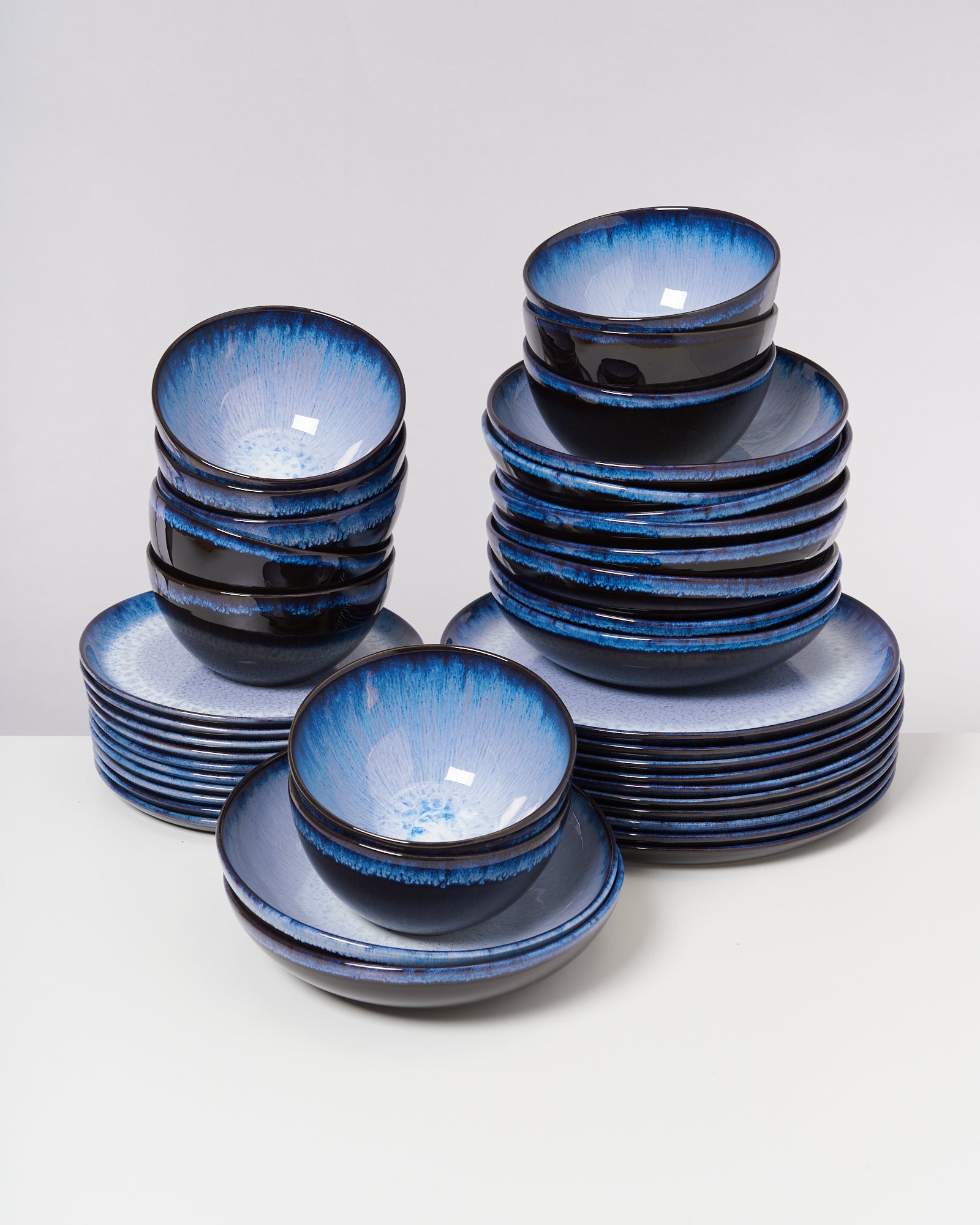 Ein Stapel von blauen Schalen und Tellern mit glasierten Rändern auf einem weißen Tisch.