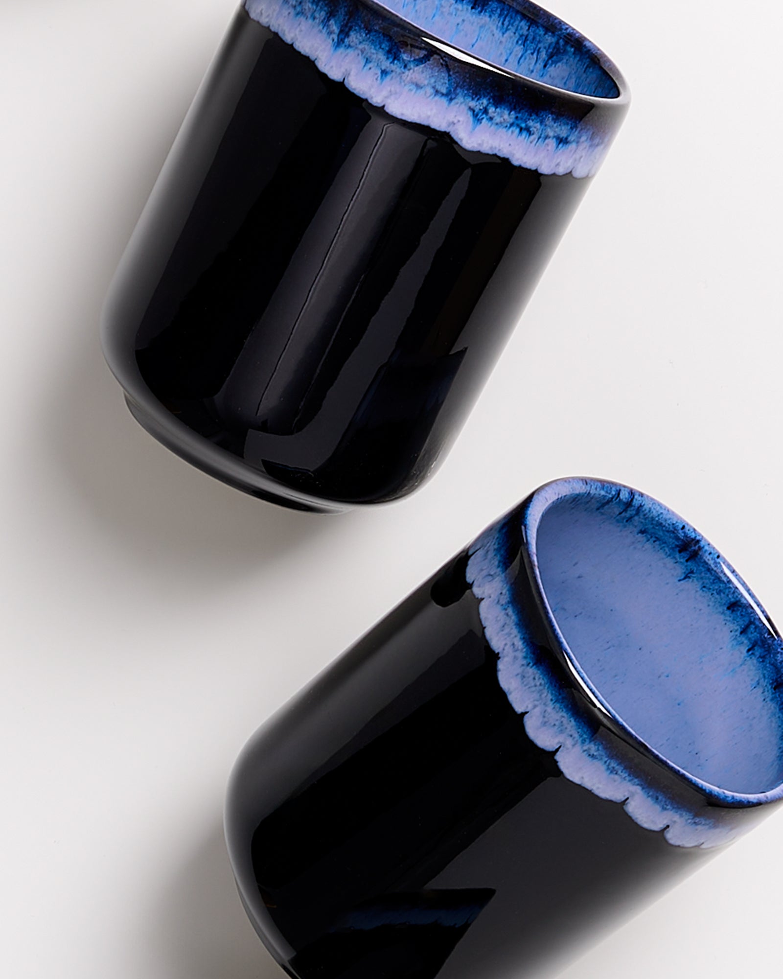 Zwei schwarze Tassen mit blauem Rand auf weißem Hintergrund.