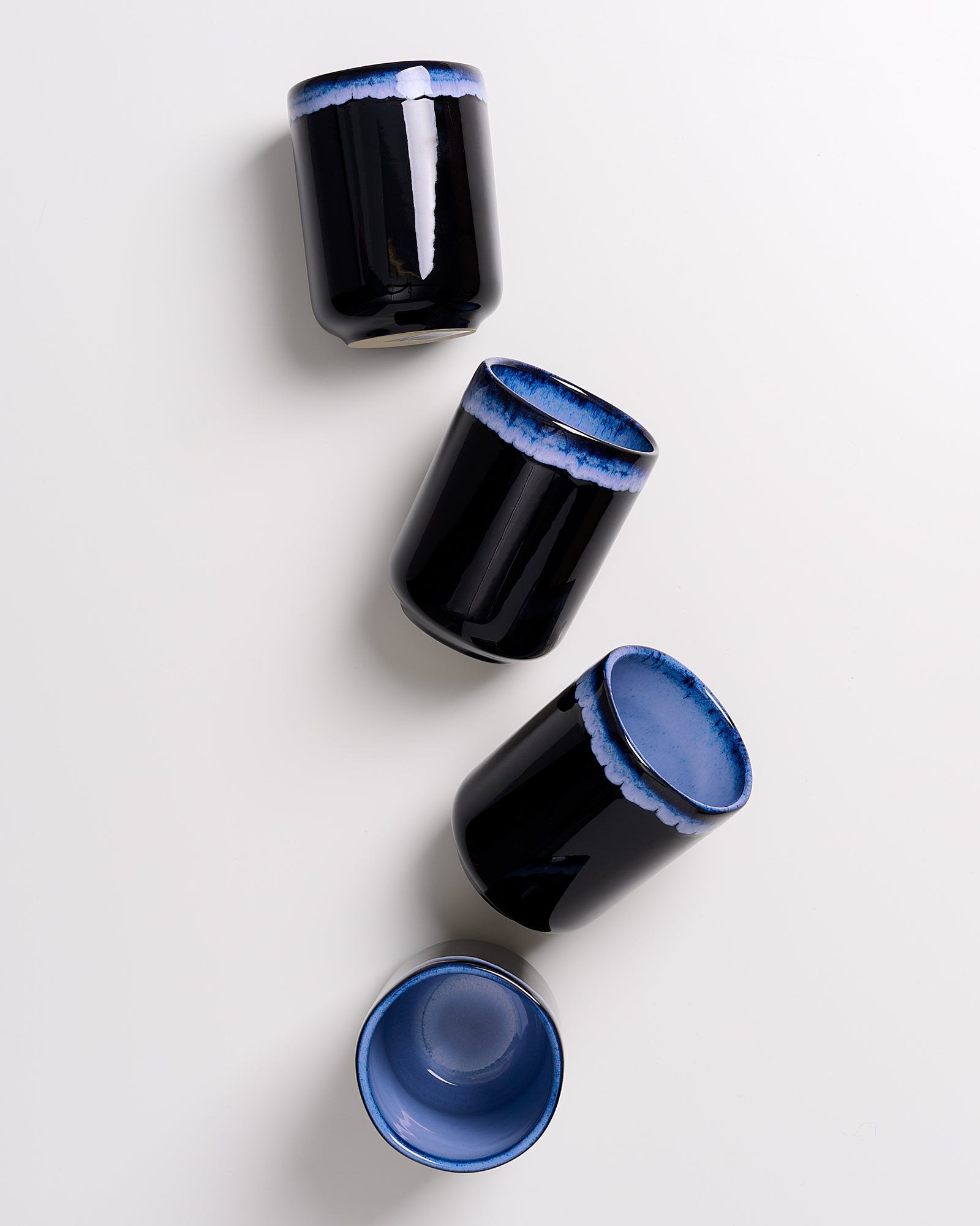 Vier schwarze Tassen mit blauem Rand stehen auf hellem Hintergrund.