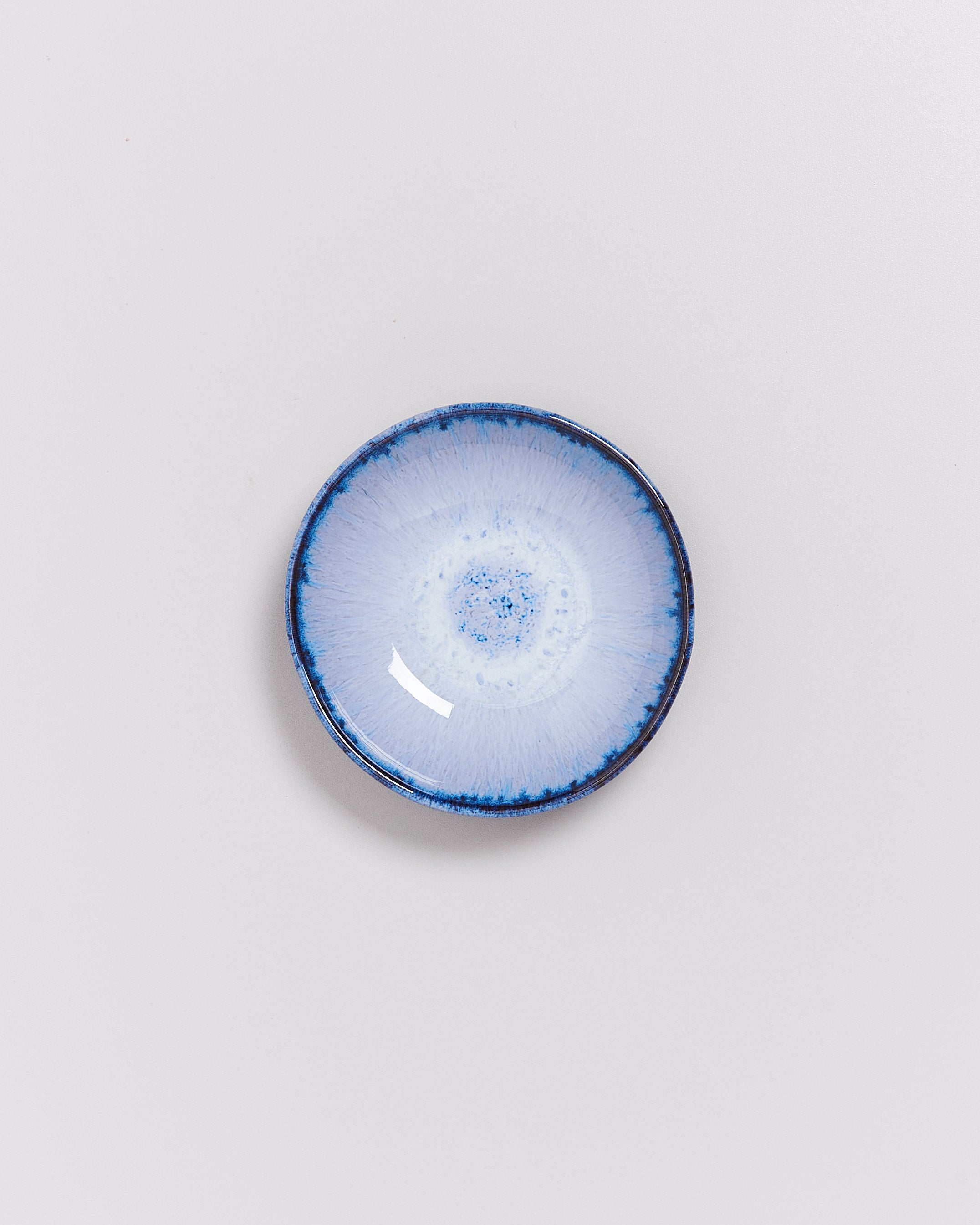 Kleine, runde, blau-weiße Keramikschale mit einem kunstvollen, strahlenförmigen Muster auf der Innenfläche.