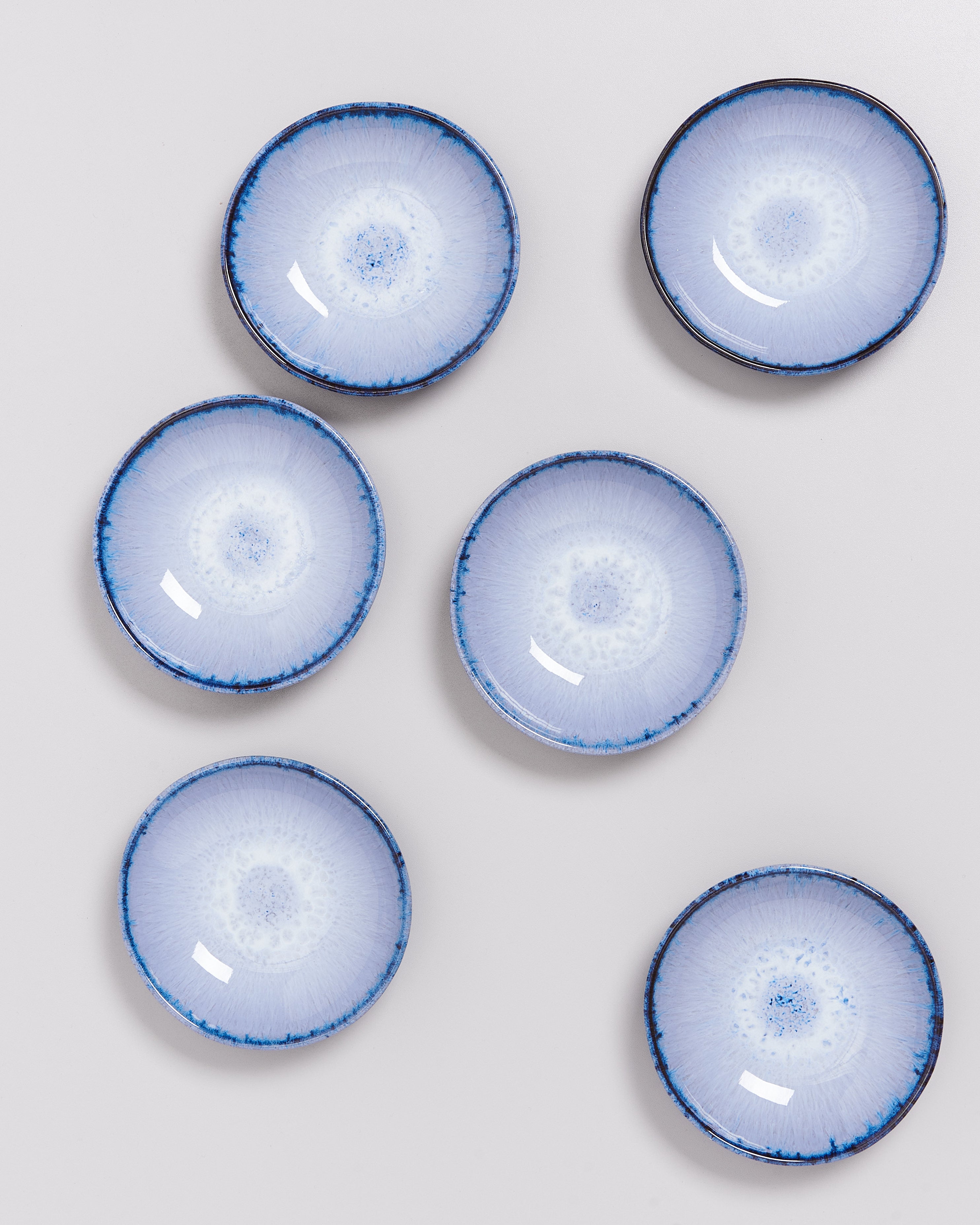 Sechs blaue Keramikteller mit weißem, radialem Muster auf einer grauen Oberfläche angeordnet.