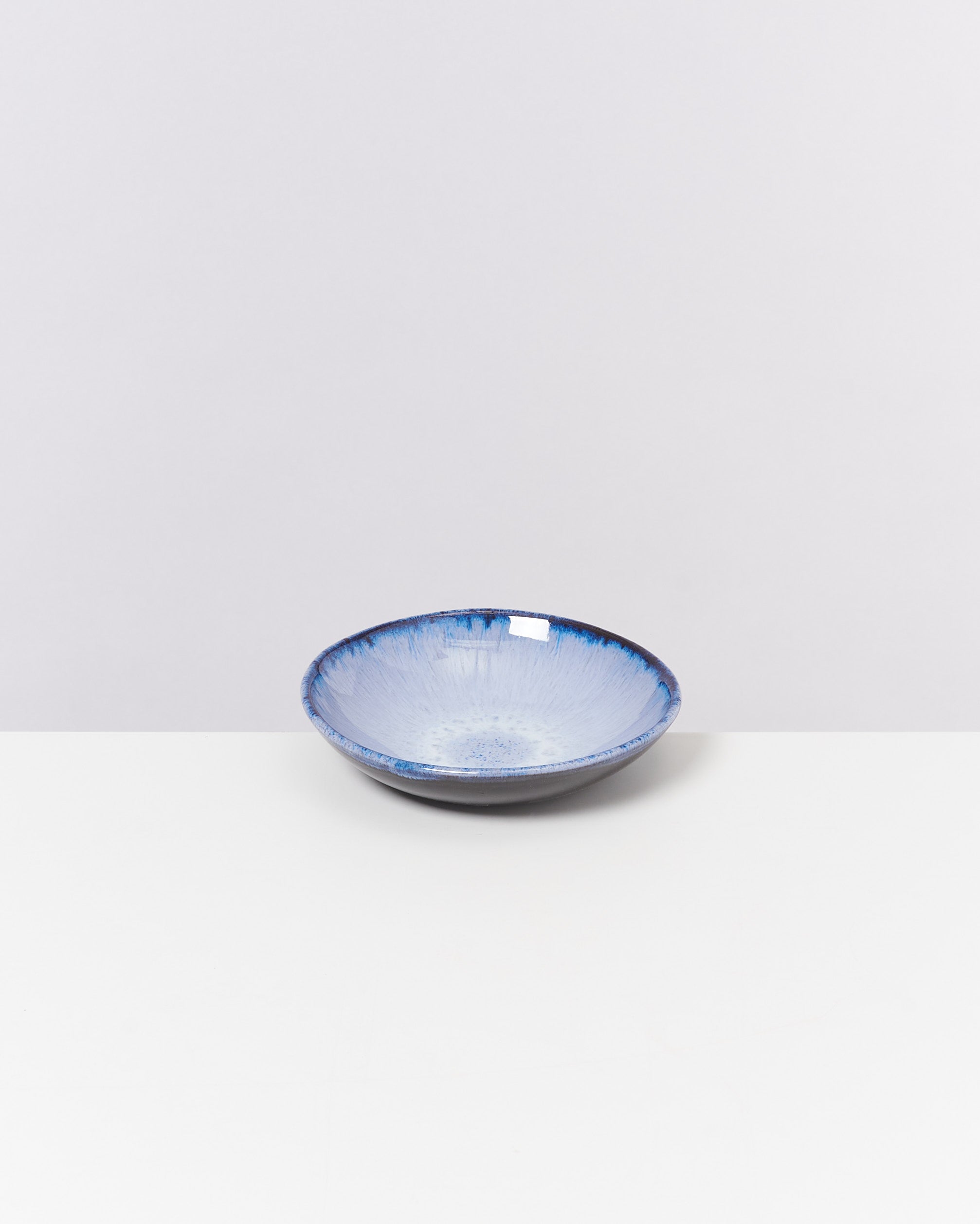 Blaue Schüssel mit weißem Innenmuster steht auf einem weißen Untergrund vor einem hellgrauen Hintergrund.