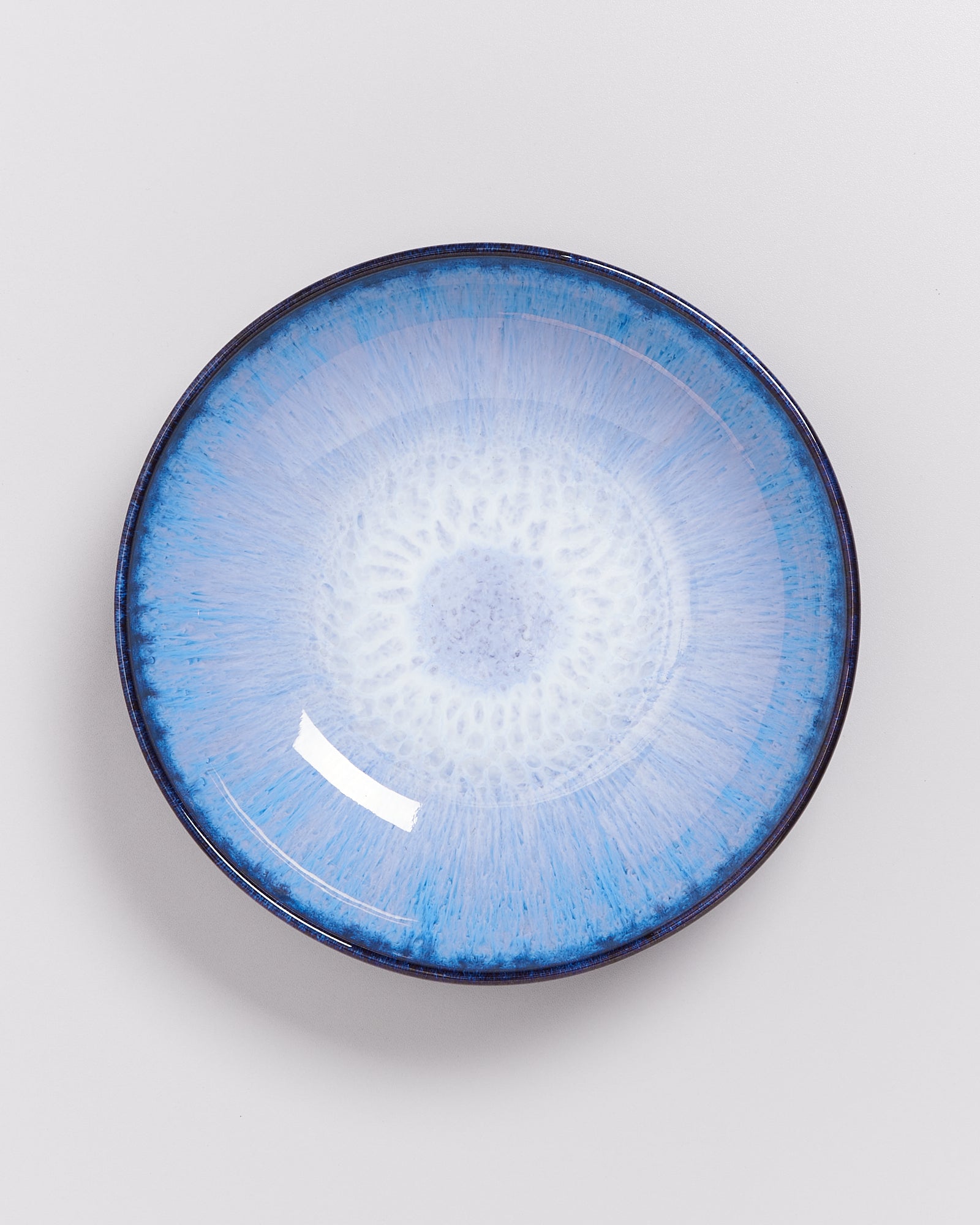 Blauer Keramikteller mit strahlendem Muster auf weißem Hintergrund.