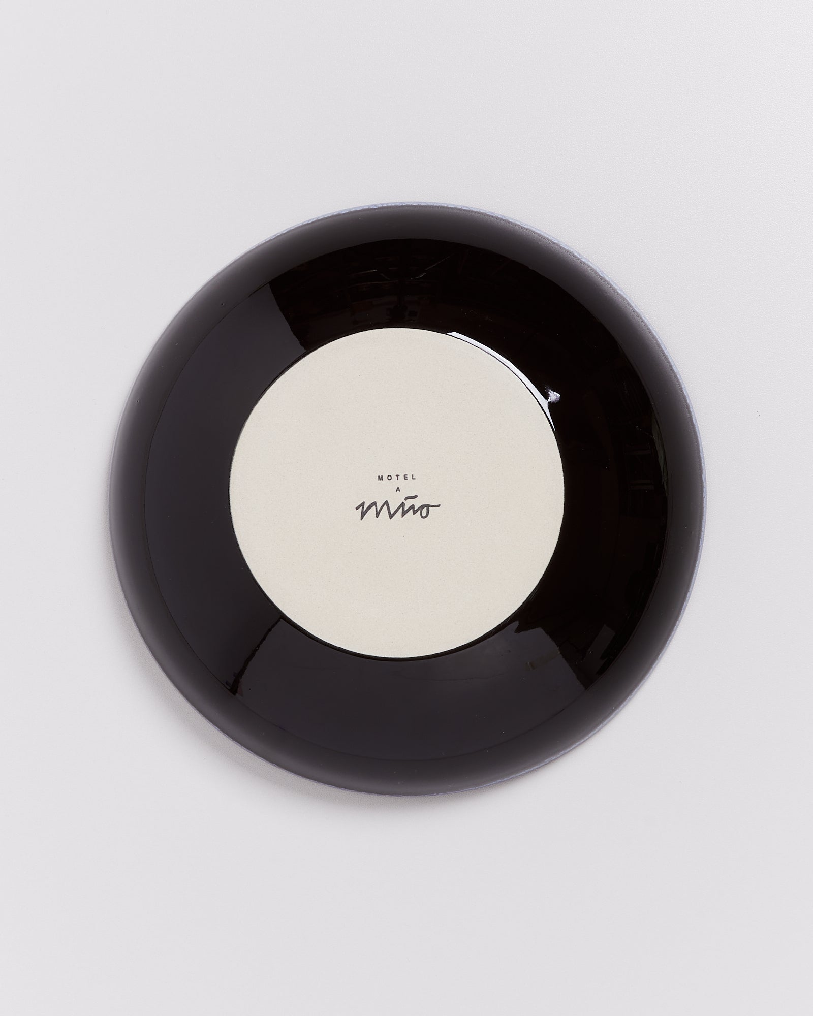 Schwarzer Teller mit cremefarbenem Zentrum und der Aufschrift "Motel a Miio".