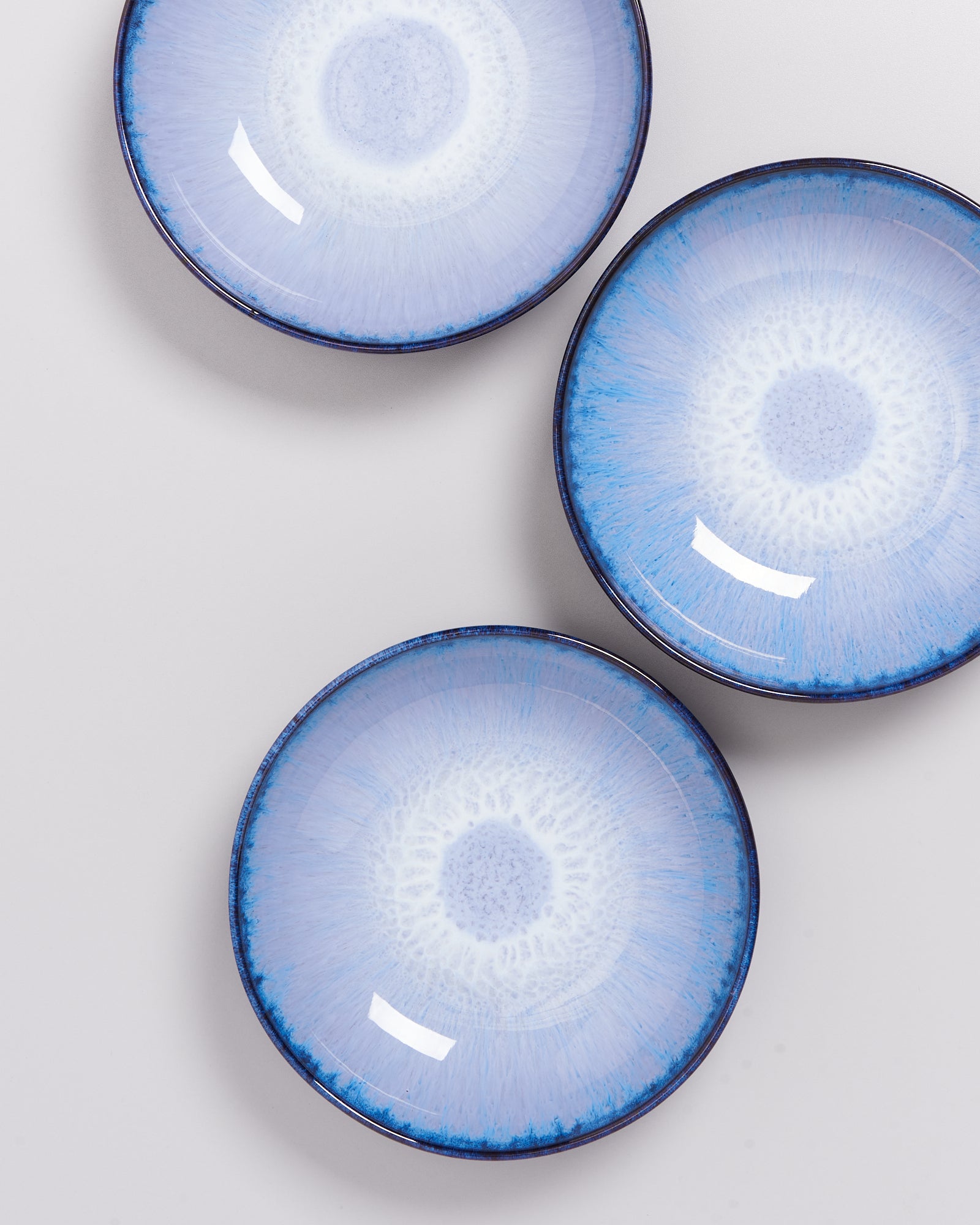 Drei blaue, runde Keramikteller mit konzentrischen Mustern liegen auf einer grauen Oberfläche.