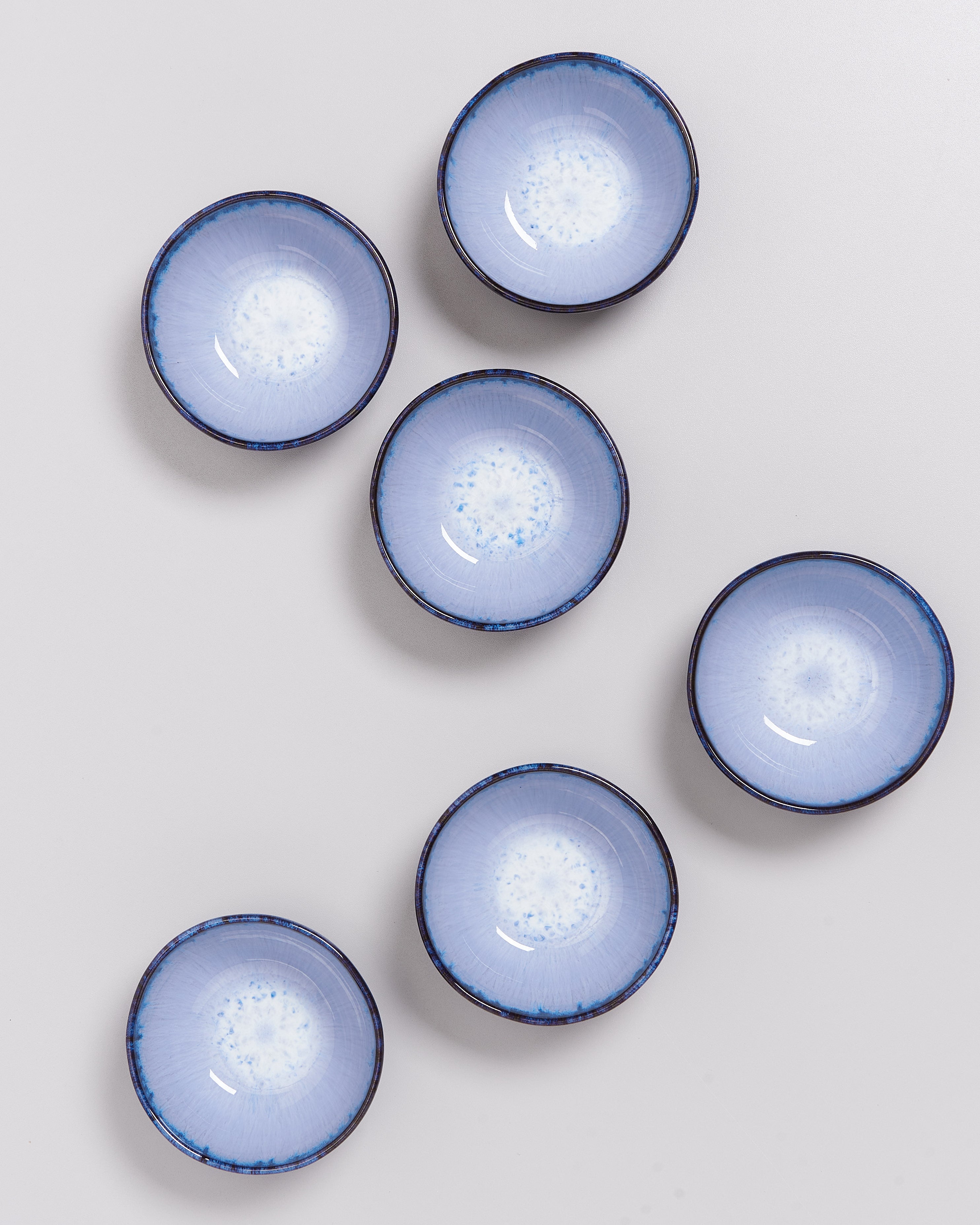 Sechs blaue Schüsseln mit dunklem Rand auf einer weißen Oberfläche angeordnet.