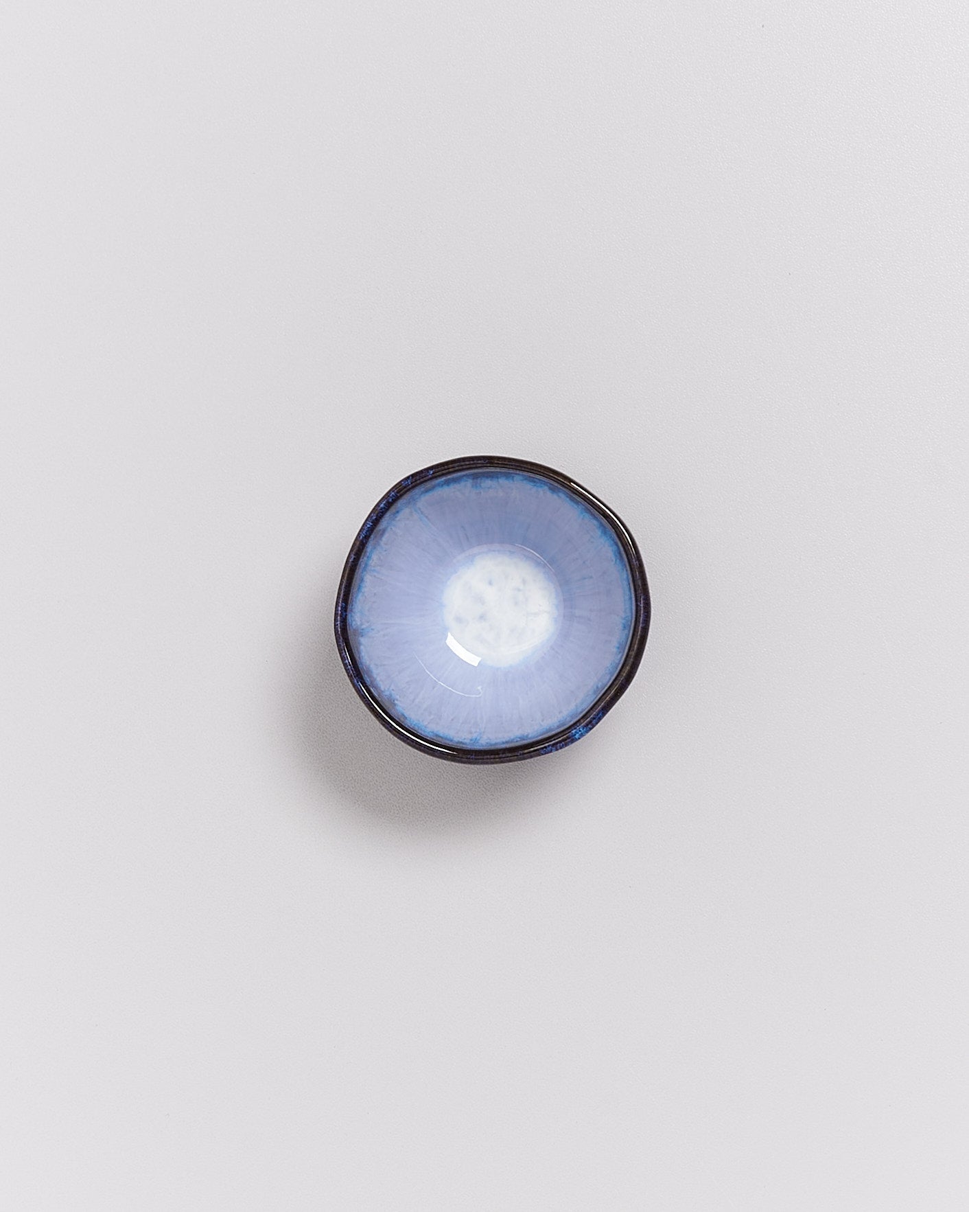 Kleine, runde, blaue Keramikschale mit einem unregelmäßigen, dunklen Rand auf einem weißen Hintergrund.