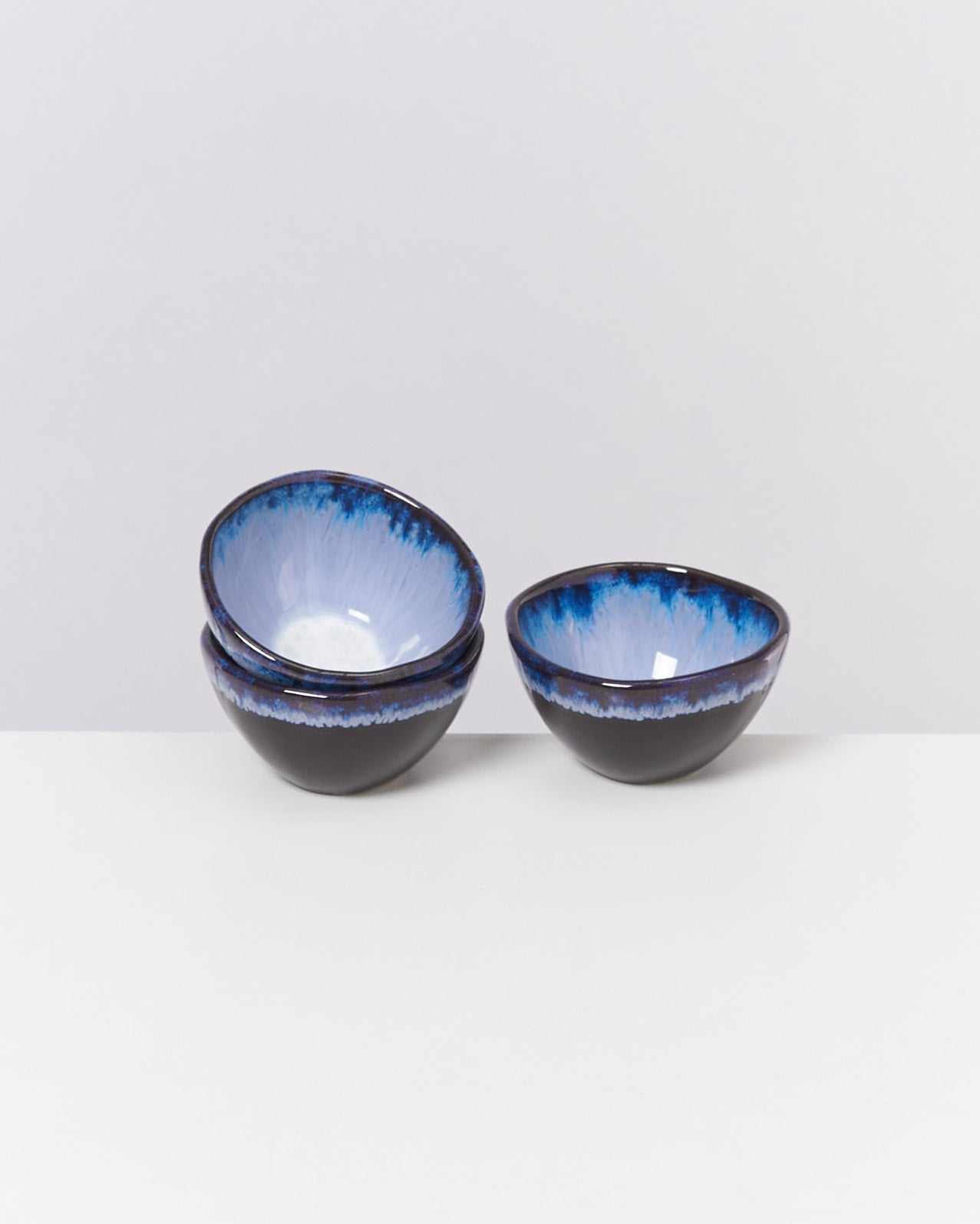 Zwei stapelbare Schalen mit blau-weißer Innenglasur und schwarzer Außenseite auf einem weißen Hintergrund.