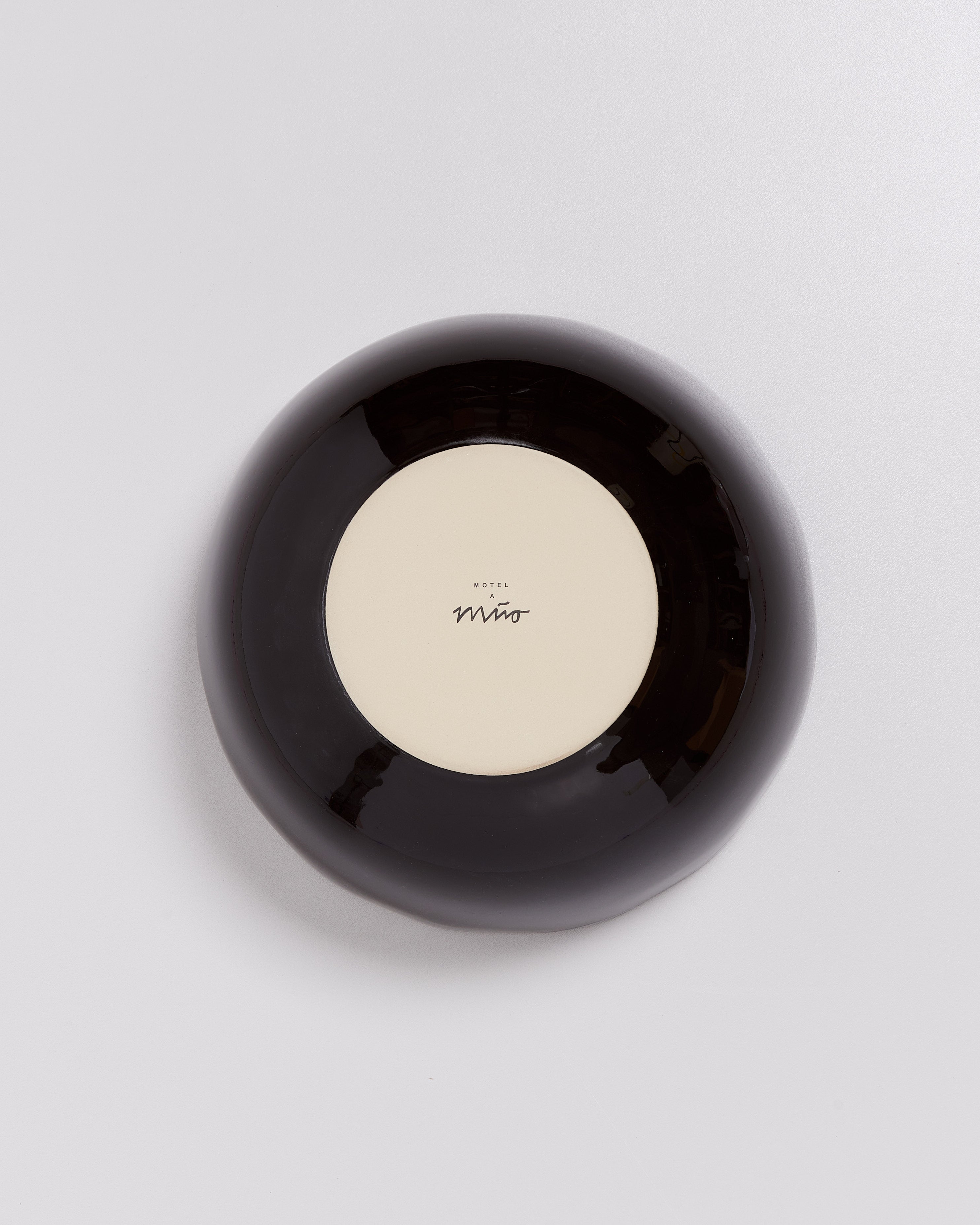 Schwarzer, runder Keramikgegenstand mit weißem Boden und Schriftzug "Motel a Mío" in der Mitte.
