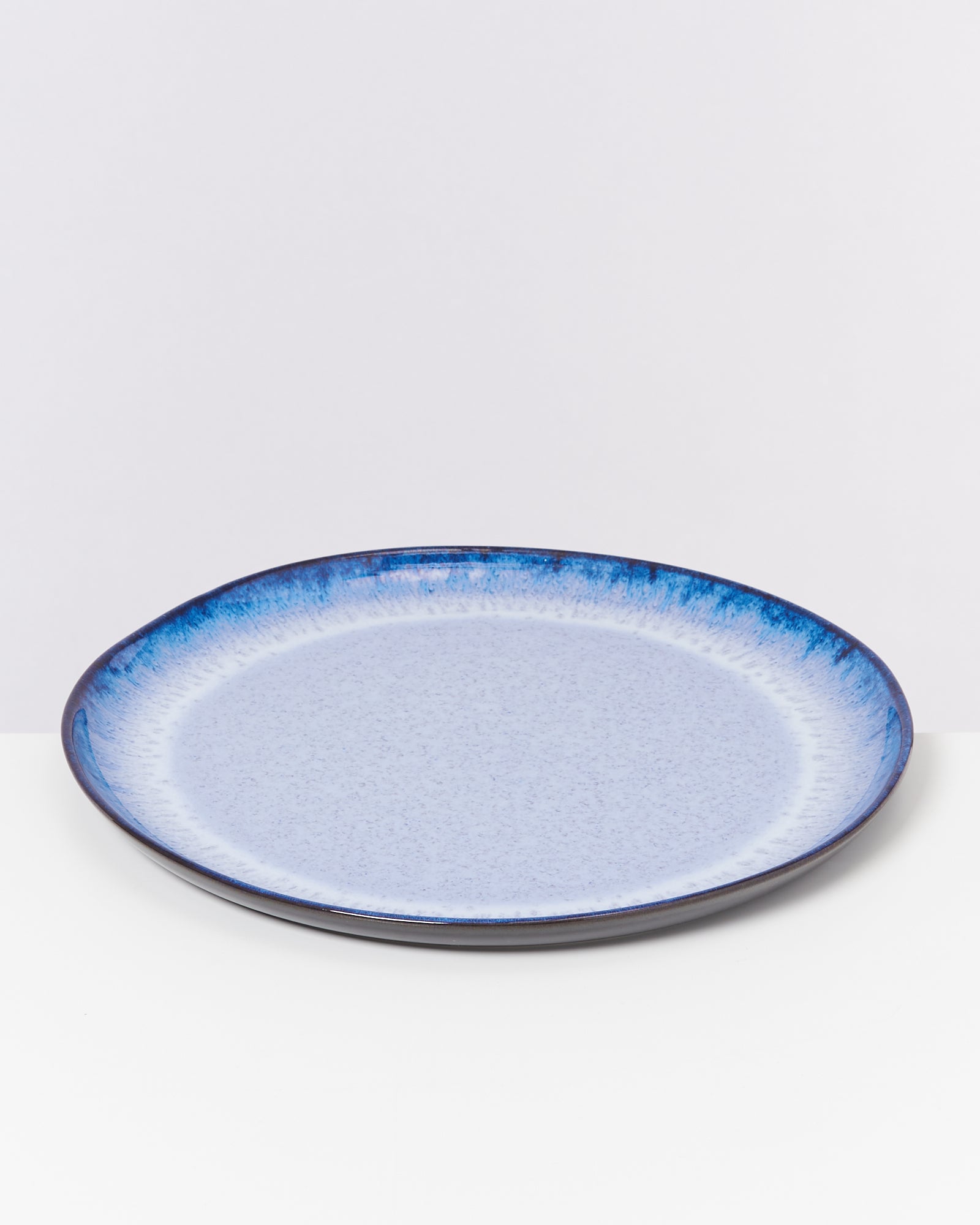 Blauer Keramikteller mit dunklem Rand auf weißem Hintergrund.