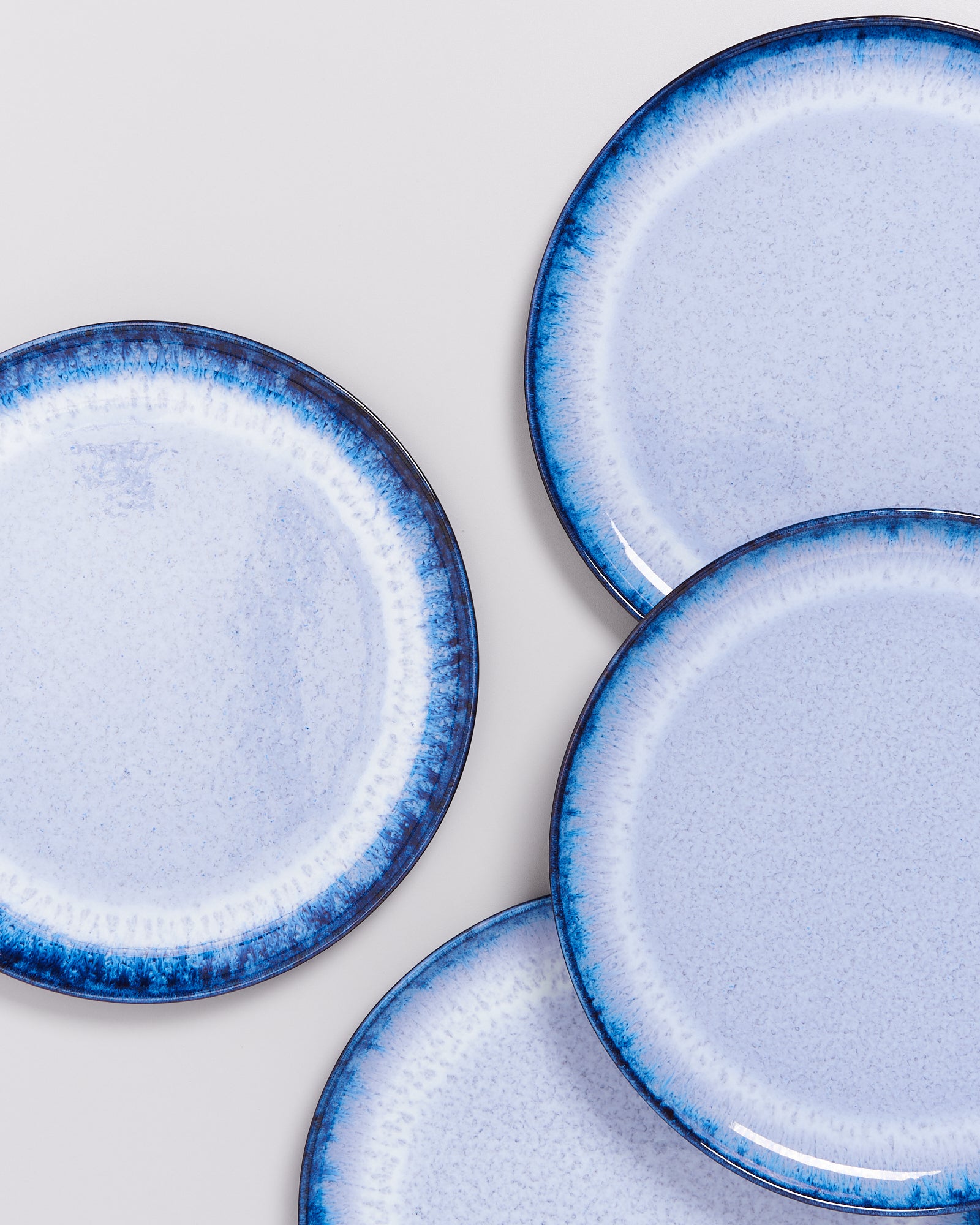Vier hellblaue Teller mit dunklem Rand auf einem hellen Hintergrund.