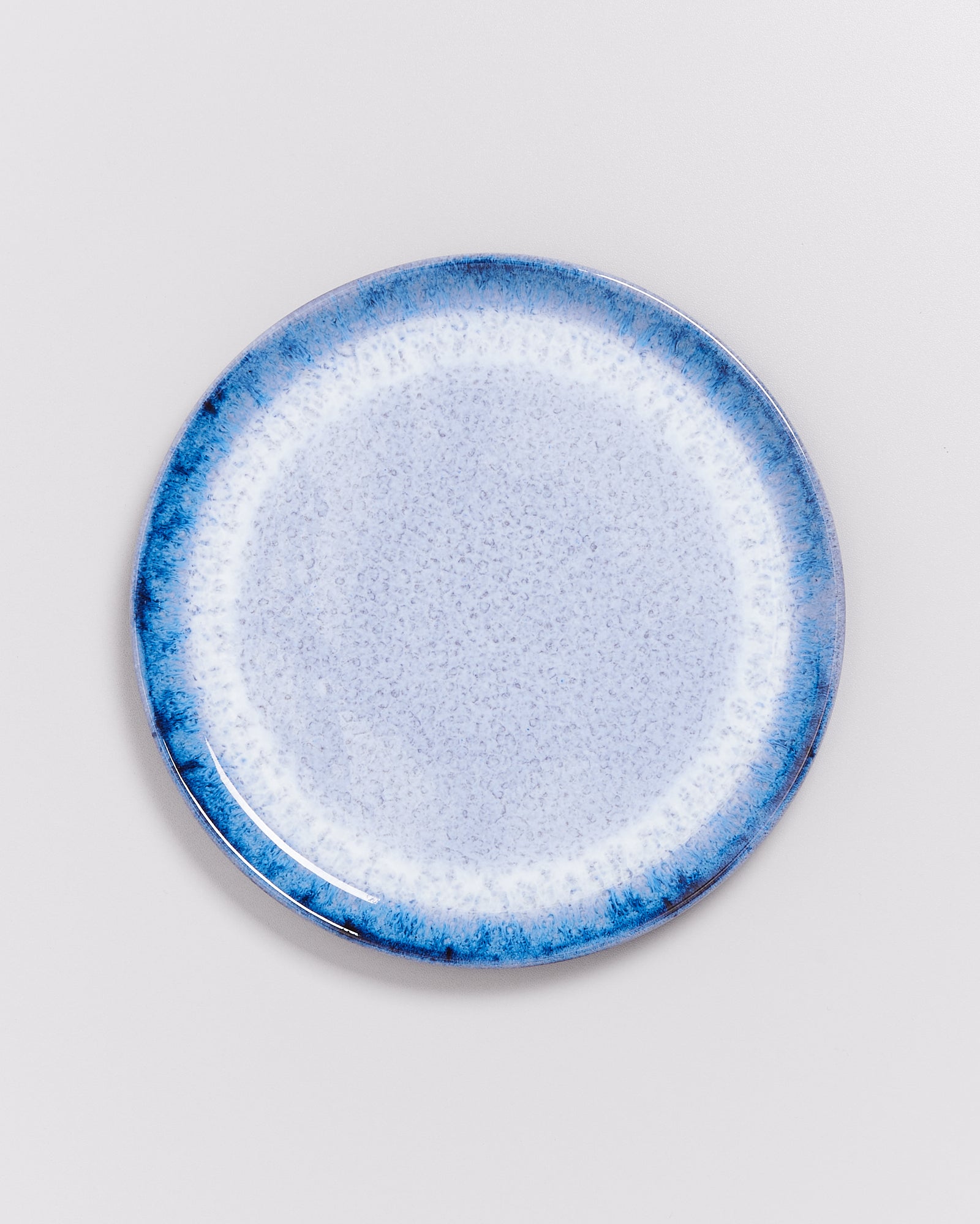 Blauer Keramikteller mit gesprenkeltem Muster auf weißem Hintergrund.