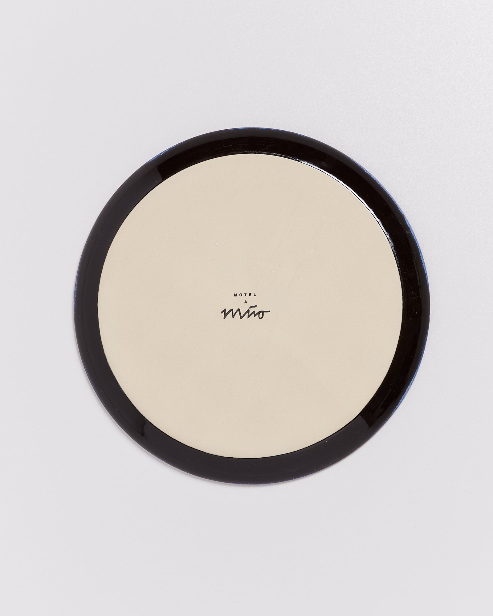 Runder, flacher Teller mit einem schwarzen Rand und schwarzer Schrift im Zentrum auf hellem Hintergrund.